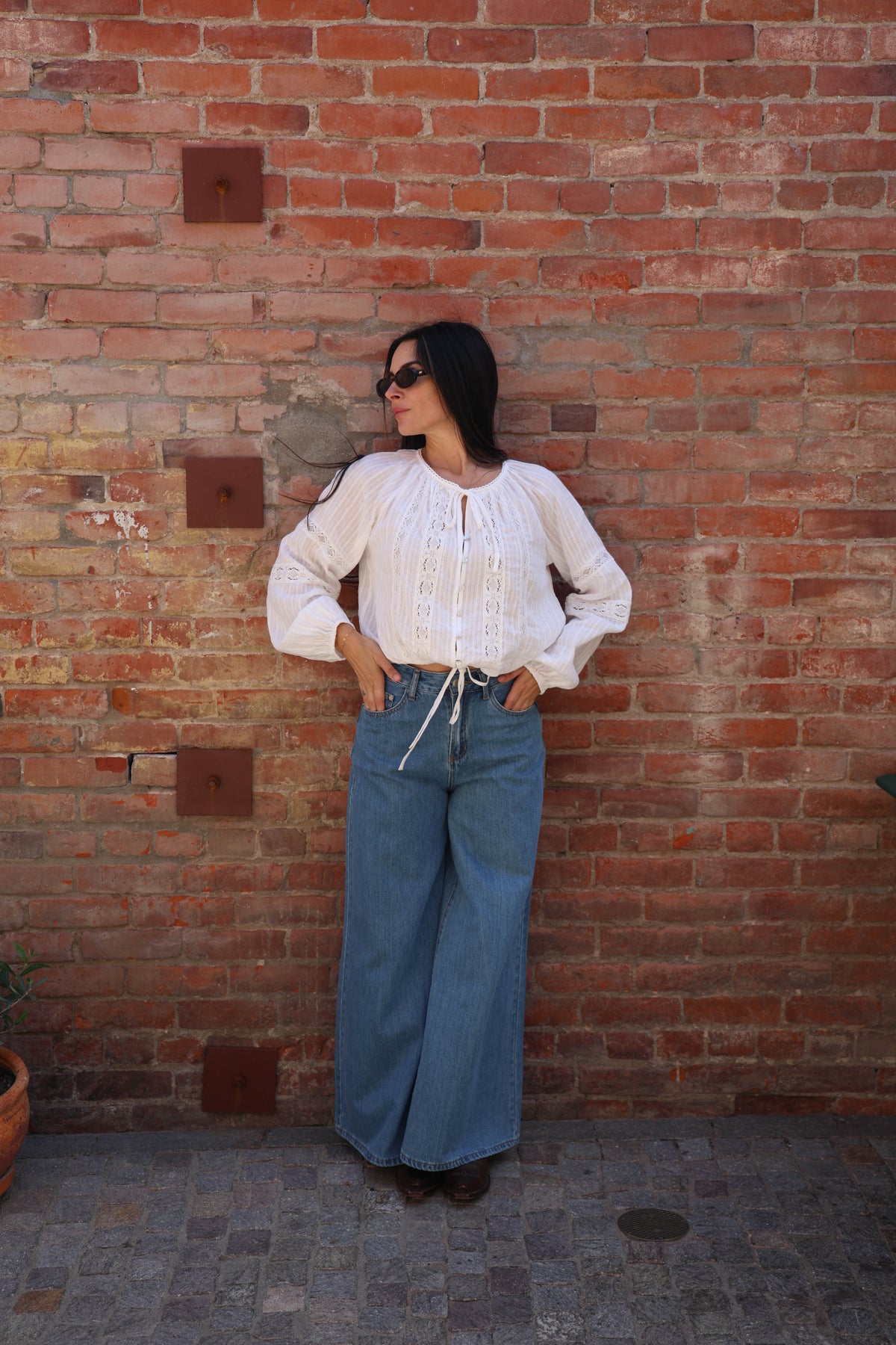 Woman wearing a white blouse and blue jeans against a brick wall.