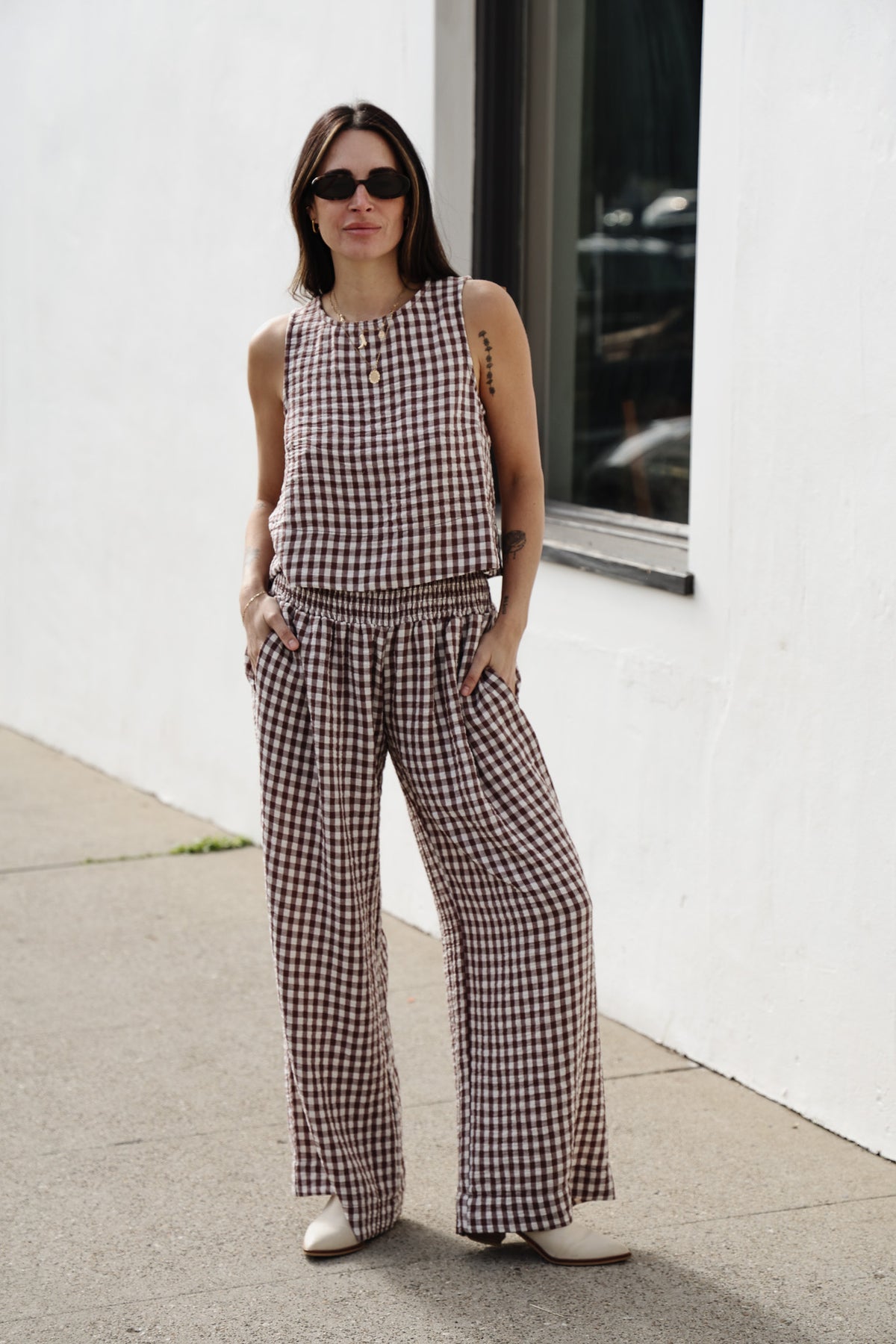 Woman wearing a checkered outfit standing against a white wall.