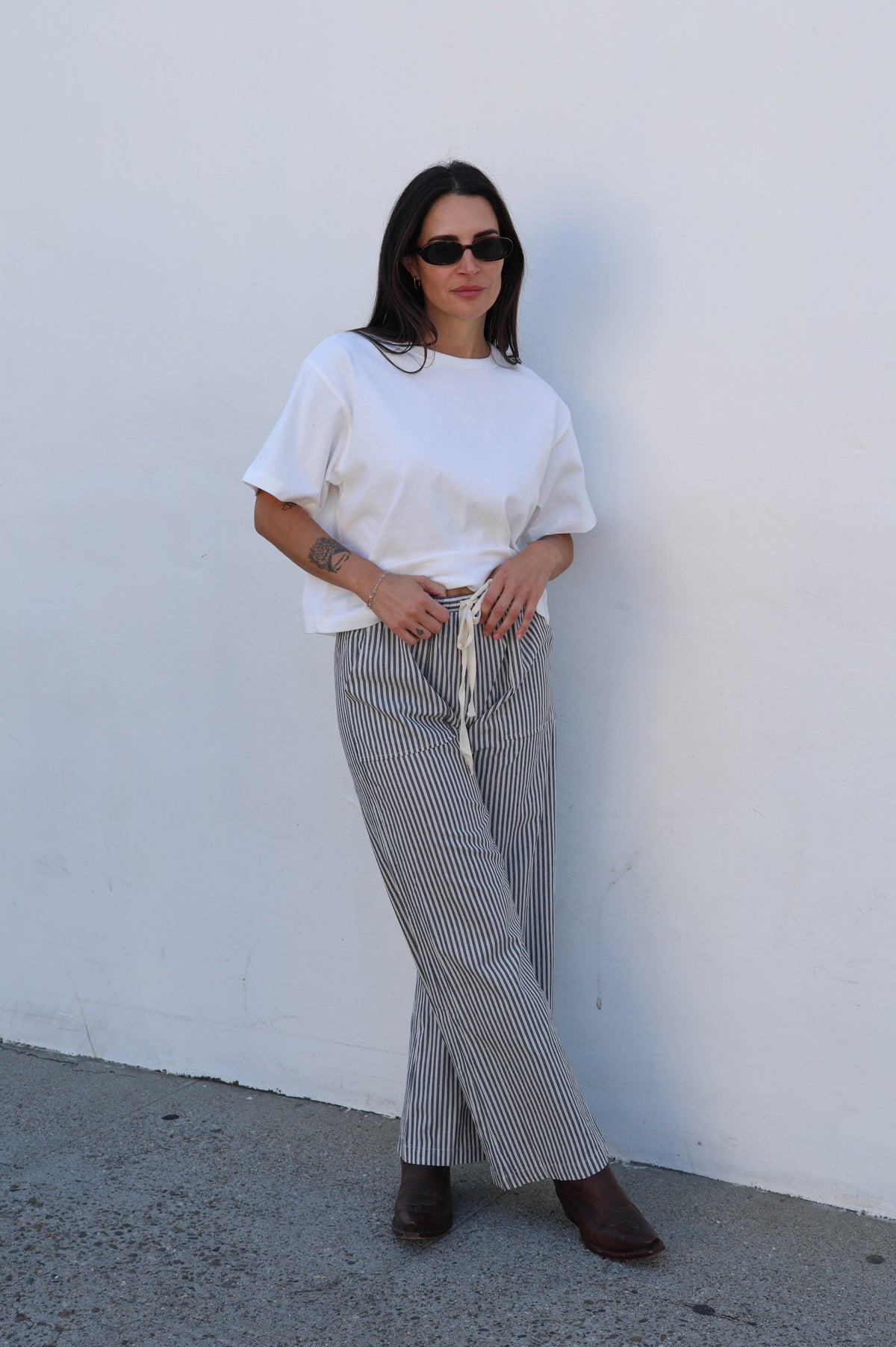 Woman wearing a white top and striped pants against a white wall.
