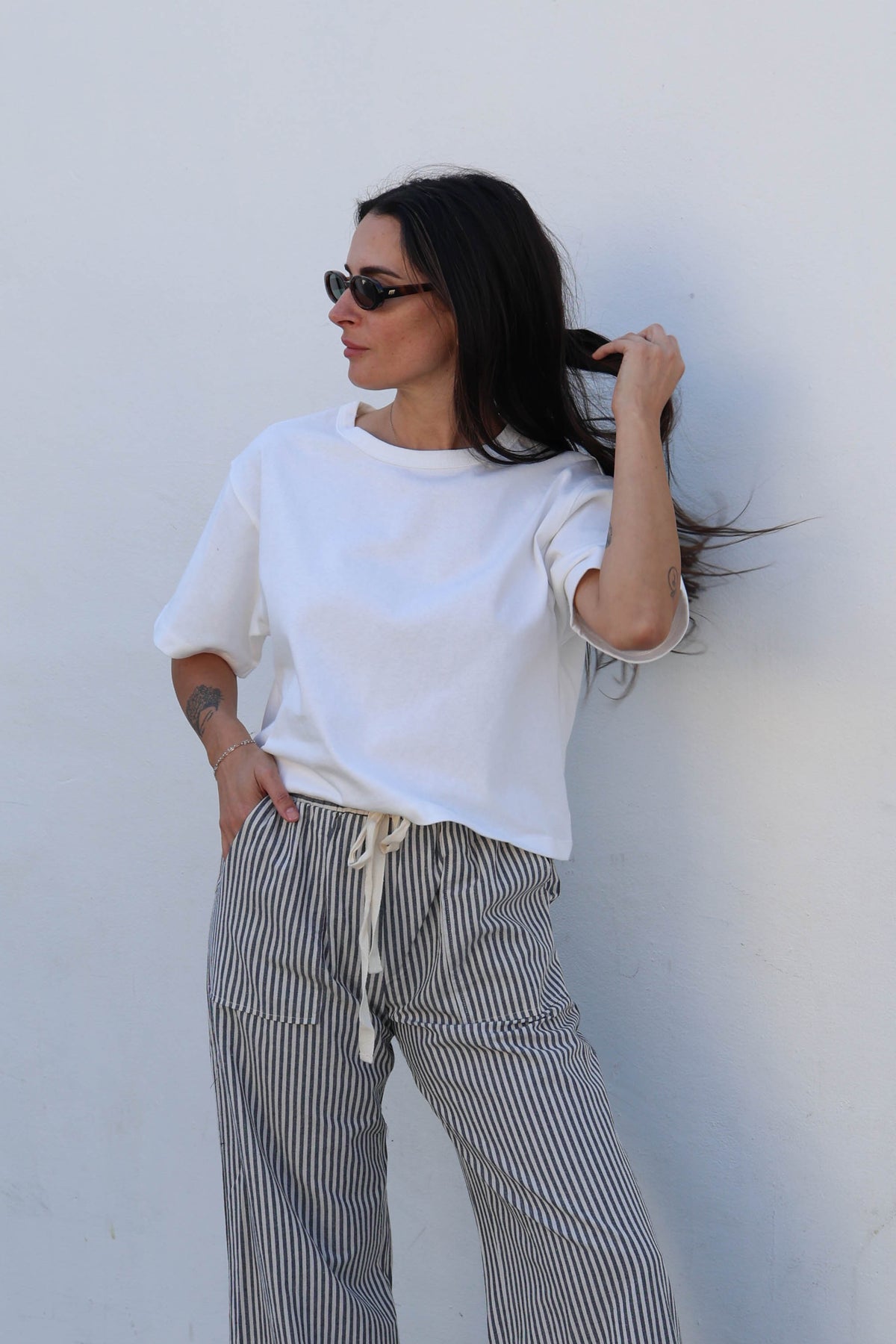 Woman wearing a white tee and striped pants against a white wall