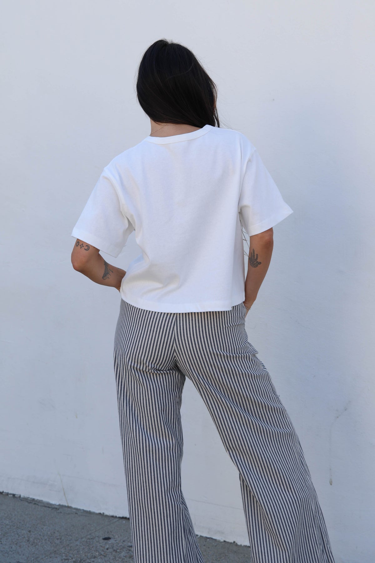 Woman wearing a white tee and striped pants against a white wall