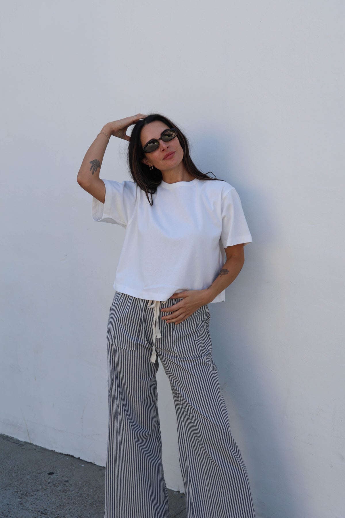 Woman wearing a white tee and striped pants against a white wall