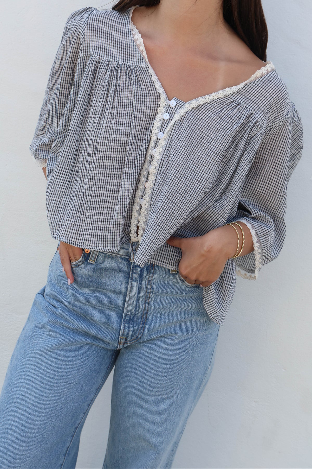 Woman wearing a plaid blouse with lace and white buttons against a white background