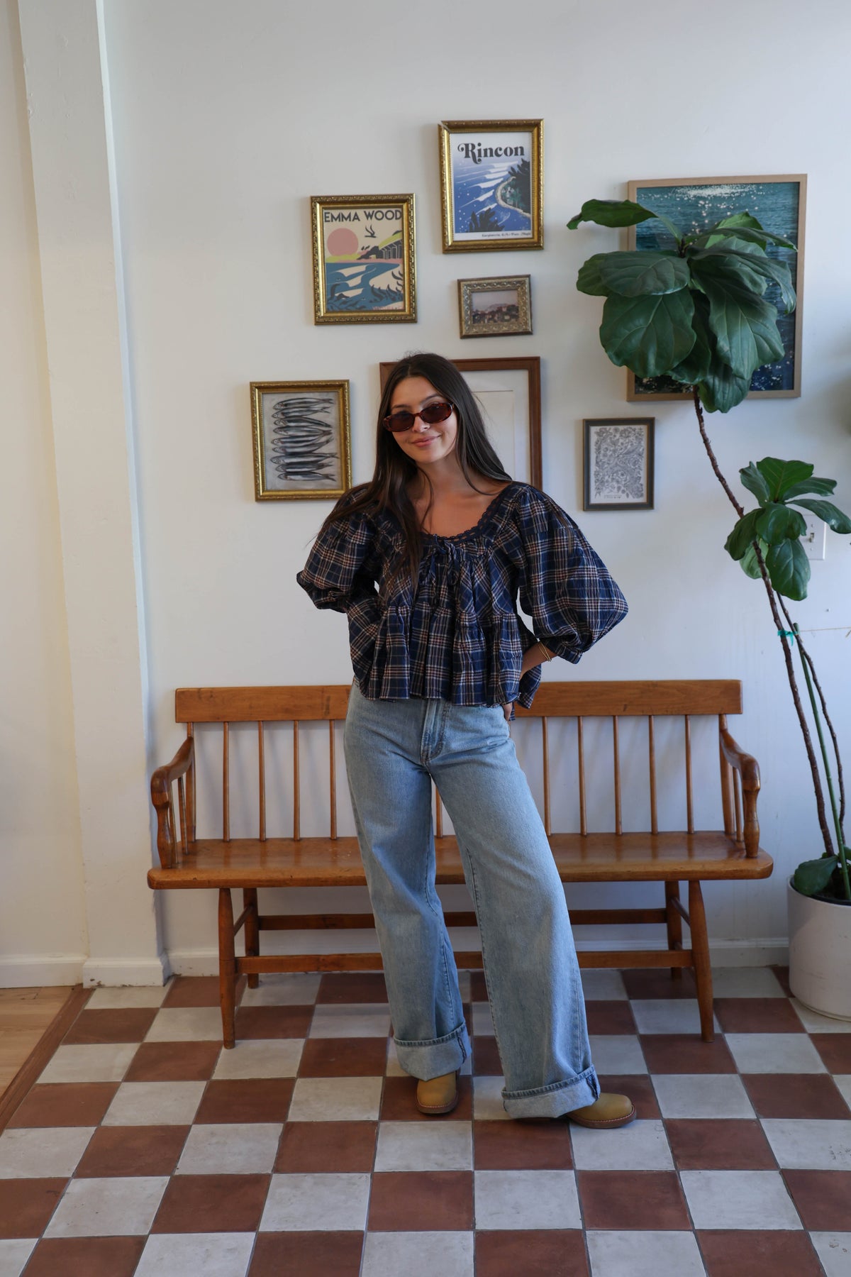 A woman wearing a navy blue plaid blouse with a ruffled neckline and tie detail, paired with light blue jeans.