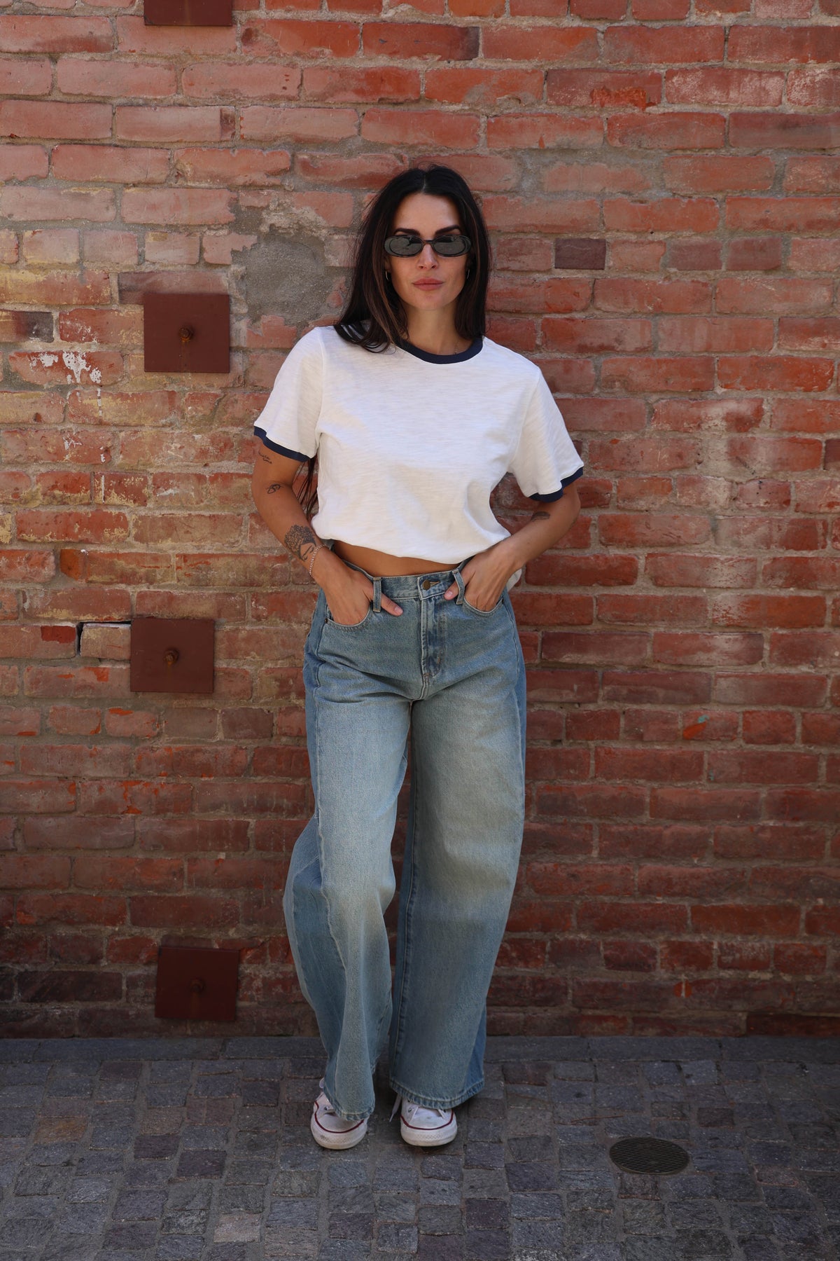 Woman wearing a white t-shirt with jeans against a brick wall.