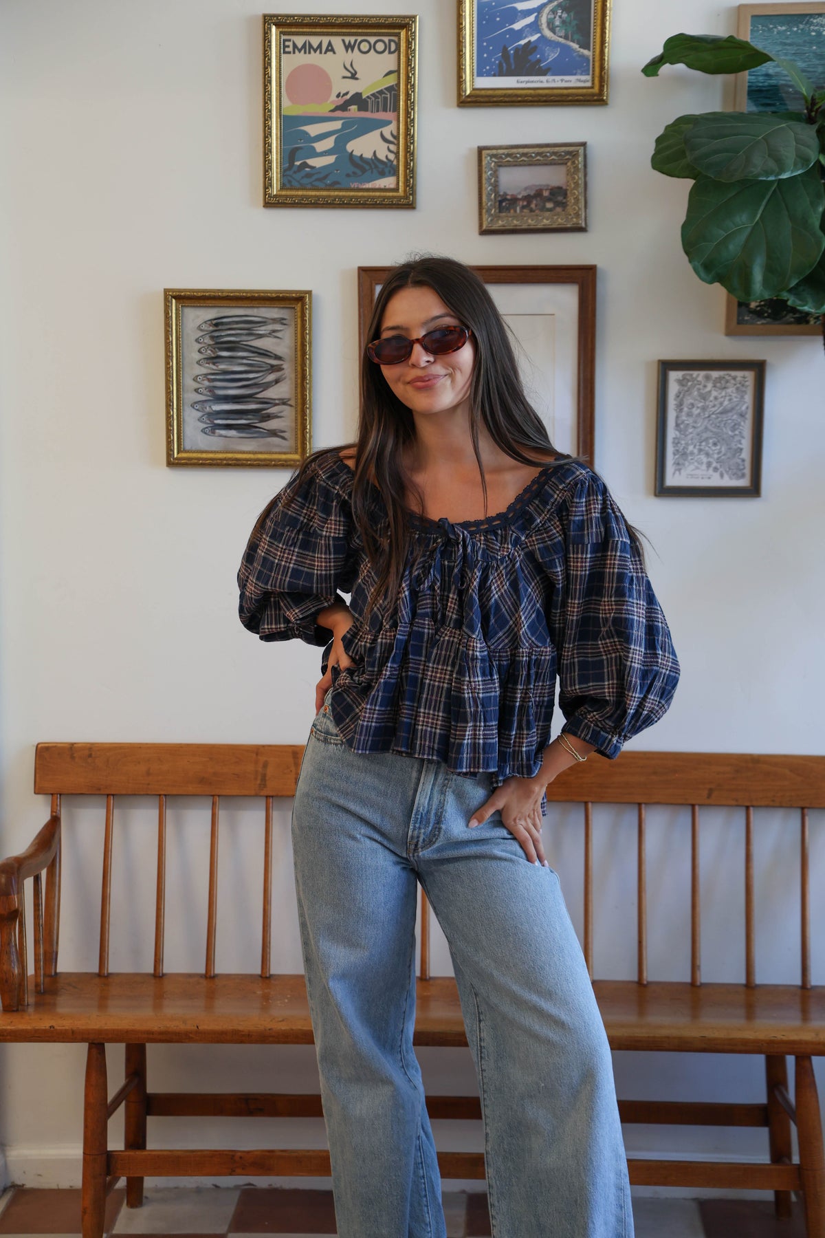 A woman wearing a navy blue plaid blouse with a ruffled neckline and tie detail, paired with light blue jeans.