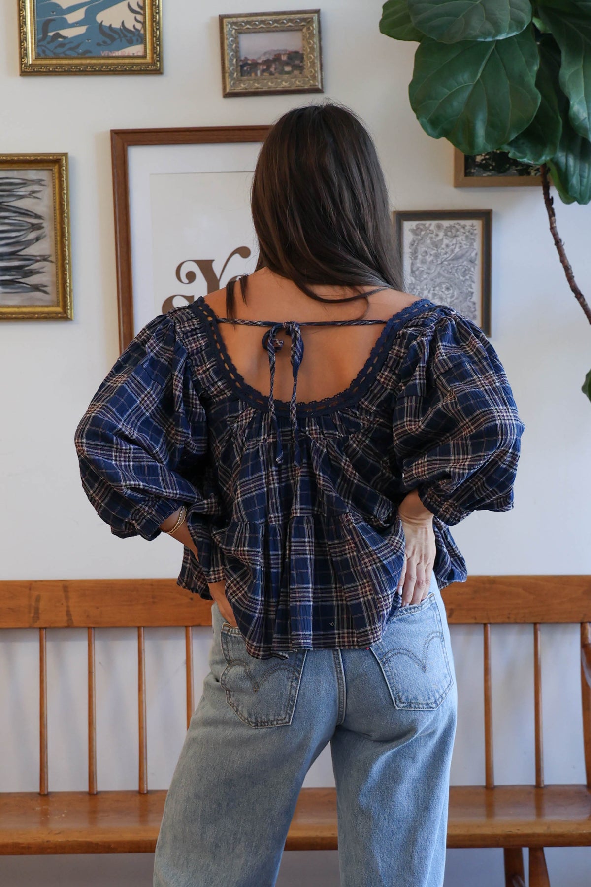 A woman wearing a navy blue plaid blouse with a ruffled neckline and tie detail, paired with light blue jeans.