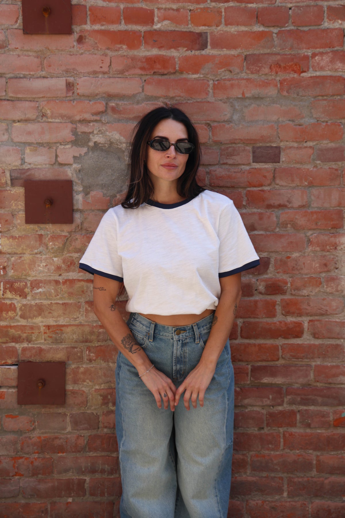 Woman wearing a white t-shirt with jeans against a brick wall.