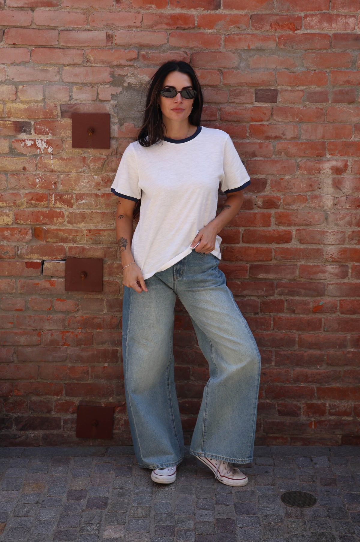 Woman wearing a white t-shirt with jeans against a brick wall.