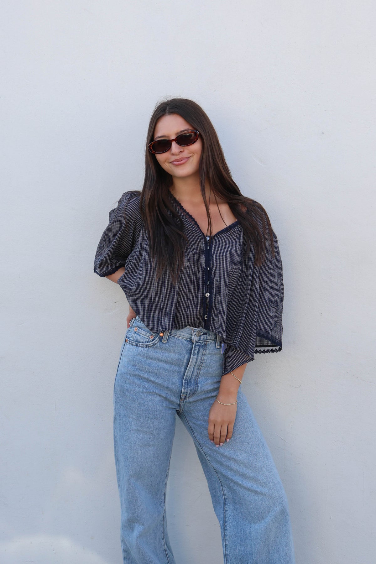 Woman wearing a blue gingham blouse with white buttons and jeans against a white background.