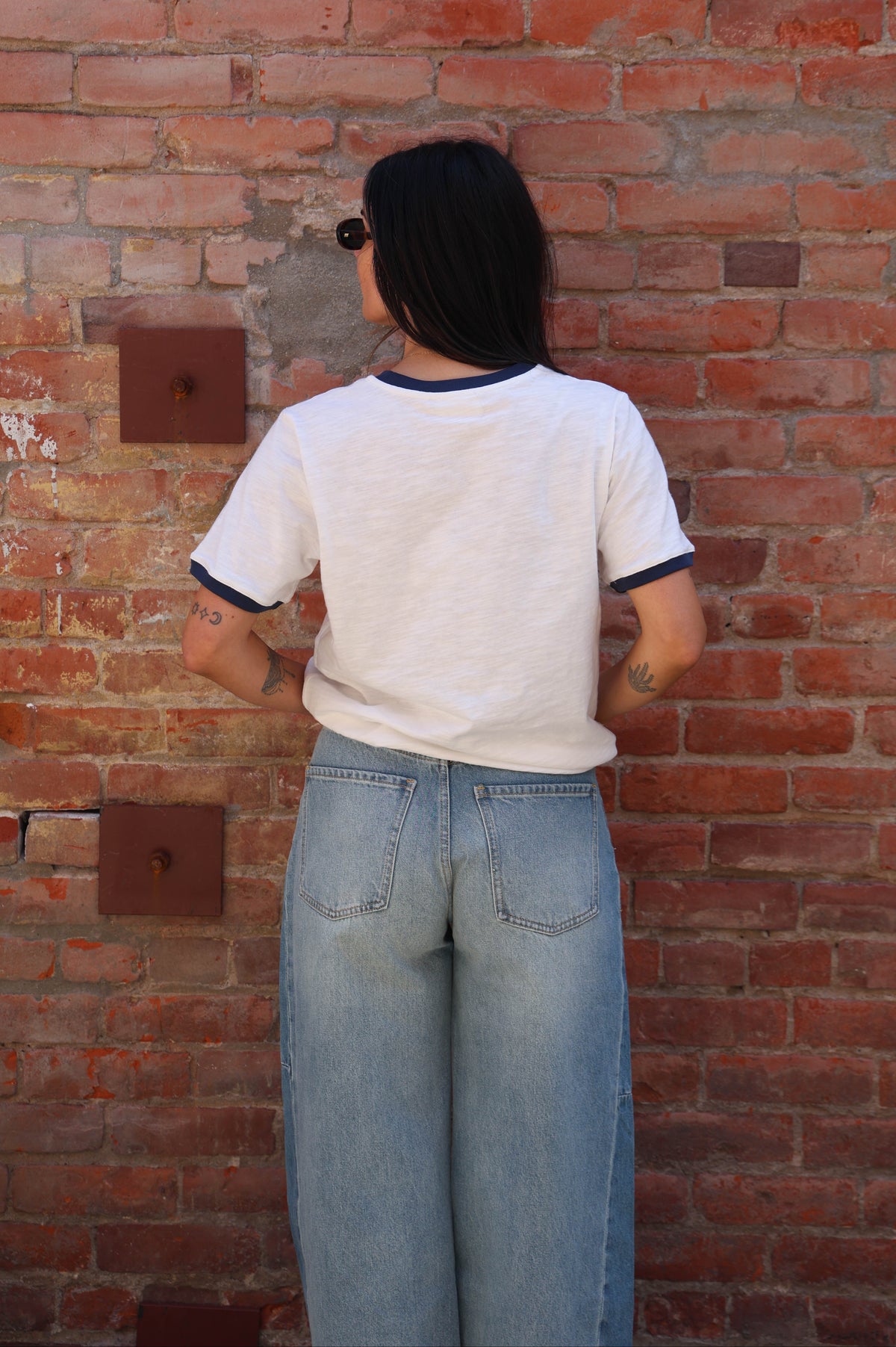 Woman wearing a white t-shirt with jeans against a brick wall.