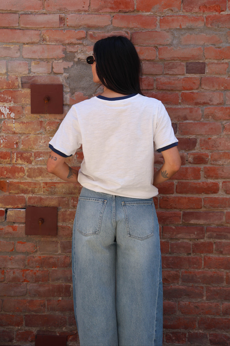 Woman wearing a white t-shirt with jeans against a brick wall.
