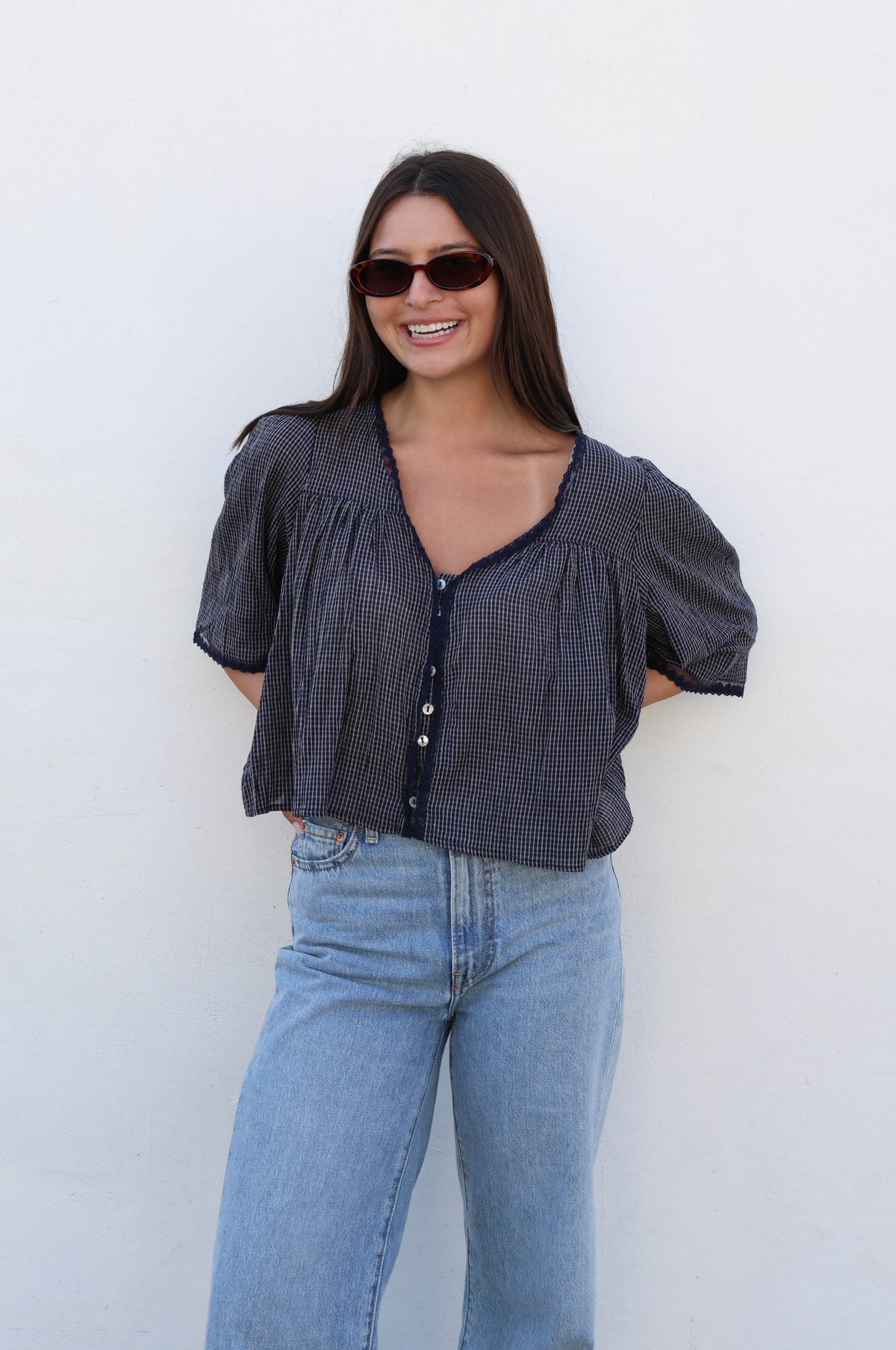 Woman wearing a blue gingham blouse with white buttons and jeans against a white background.