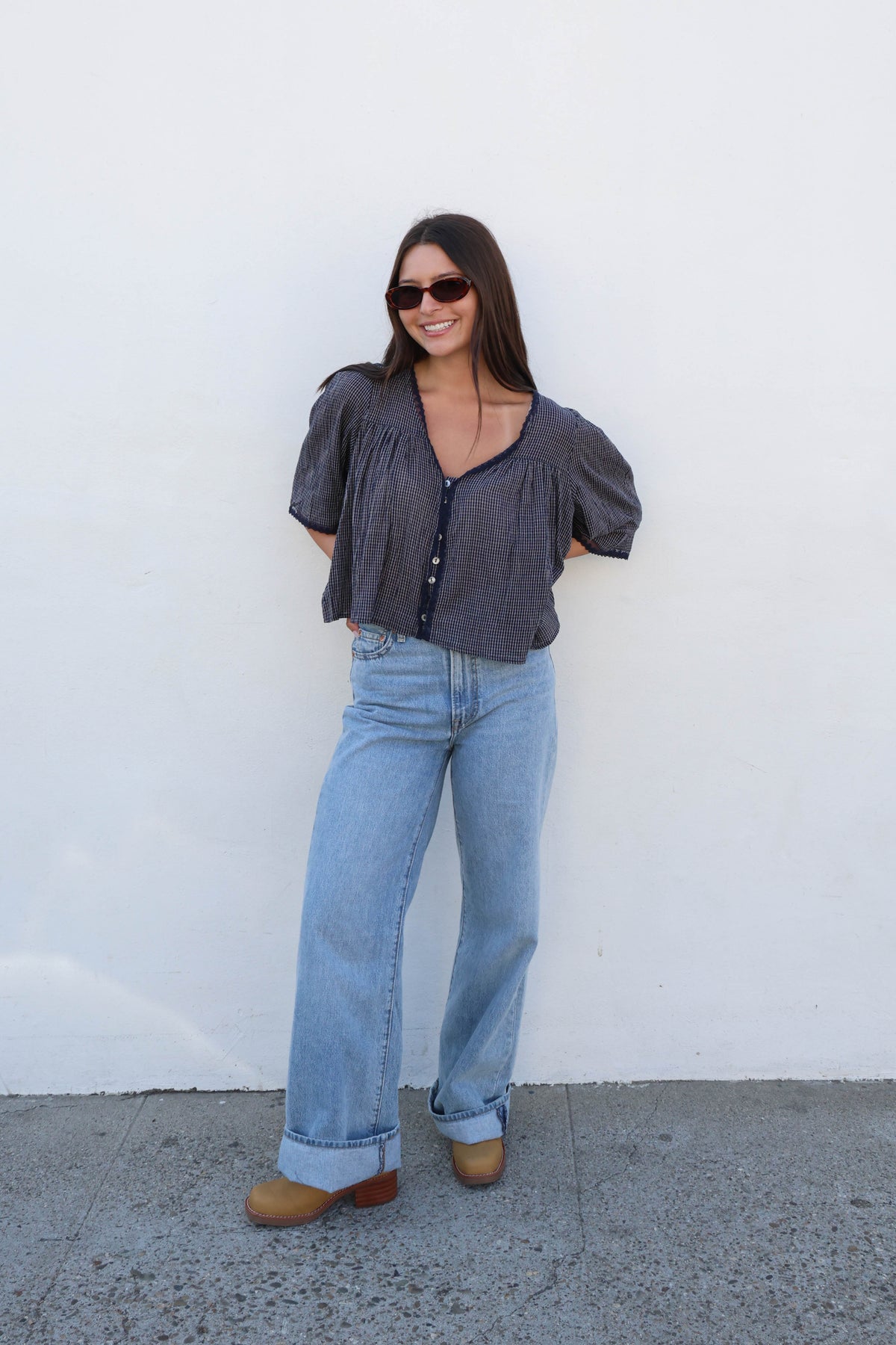 Woman wearing a blue gingham blouse with white buttons and jeans against a white background.