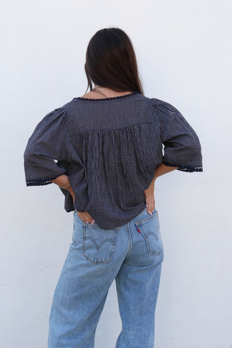 Woman wearing a blue gingham blouse with white buttons and jeans against a white background.
