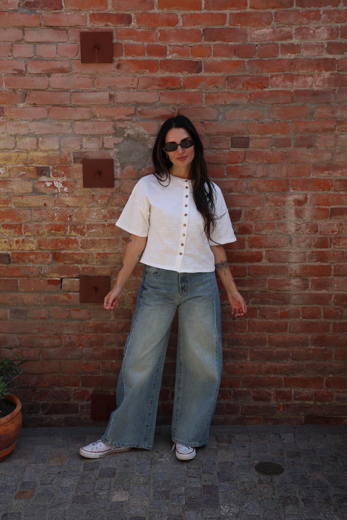 Woman wearing a white shirt with buttons and jeans against a brick wall