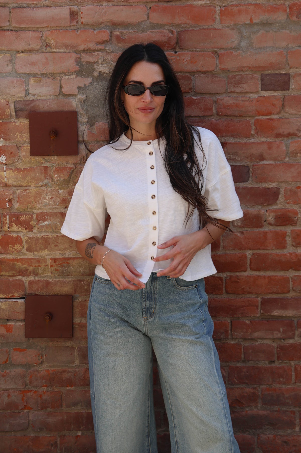 Woman wearing a white blouse and blue jeans standing against a brick wall.