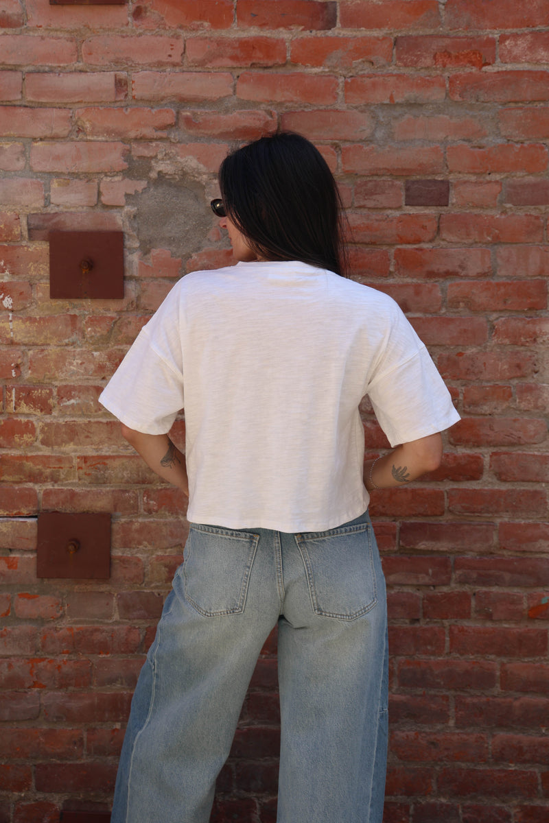 Woman wearing a white shirt with buttons and jeans against a brick wall