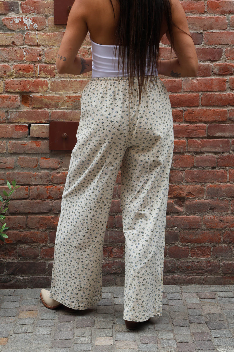 Person wearing a white floral dress standing against a brick wall.