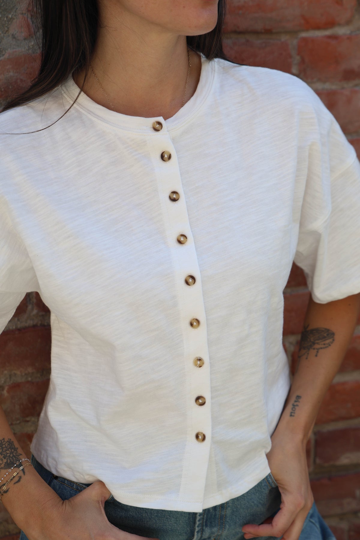 Woman wearing a white shirt with buttons and jeans against a brick wall