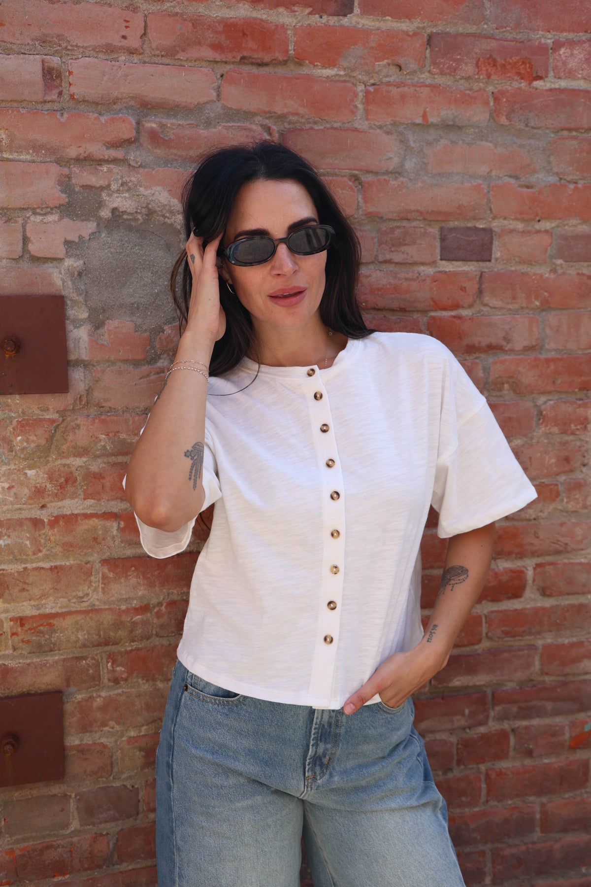 Woman wearing a white shirt with buttons and jeans against a brick wall