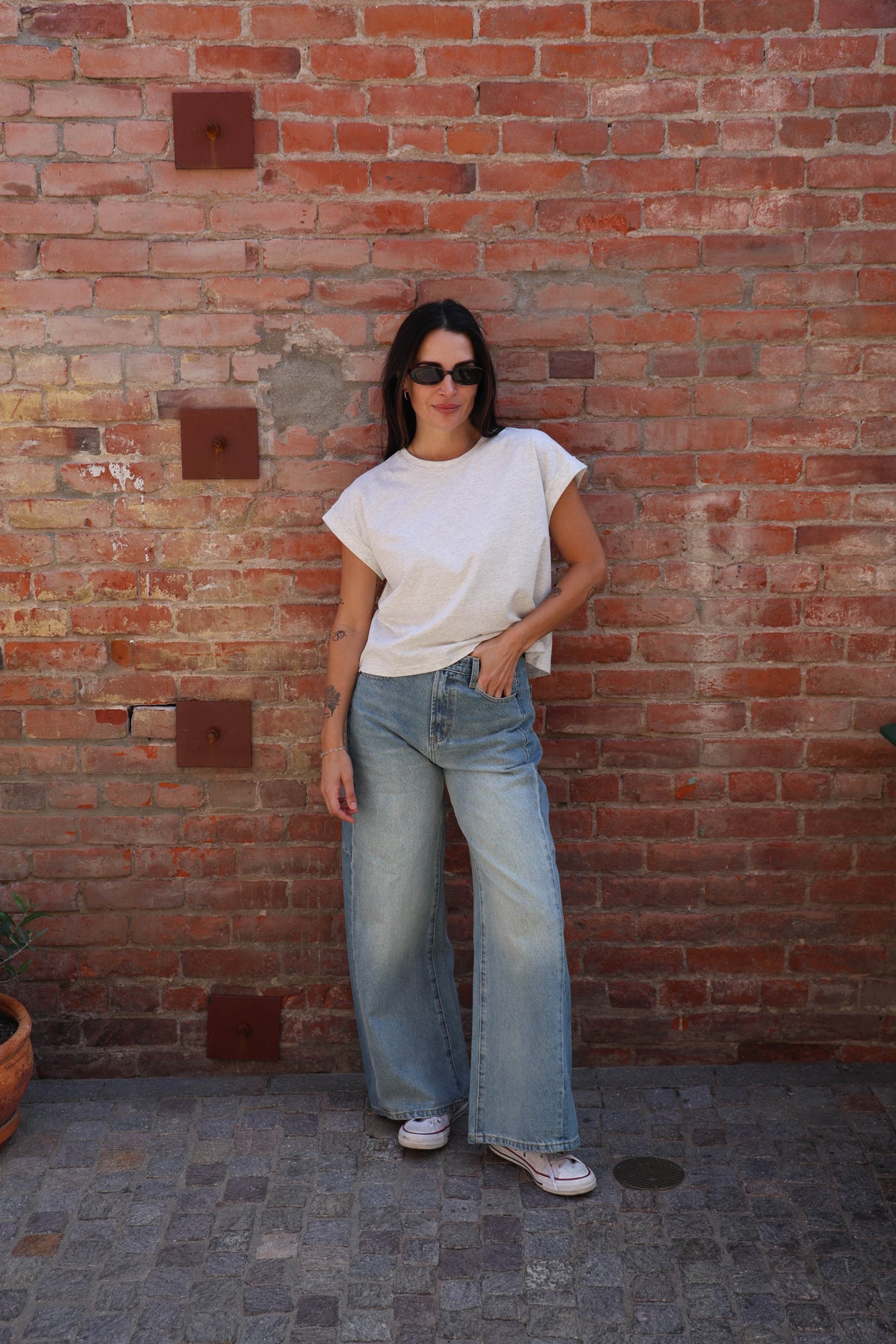 Woman wearing a great shirt with jeans against a brick wall.