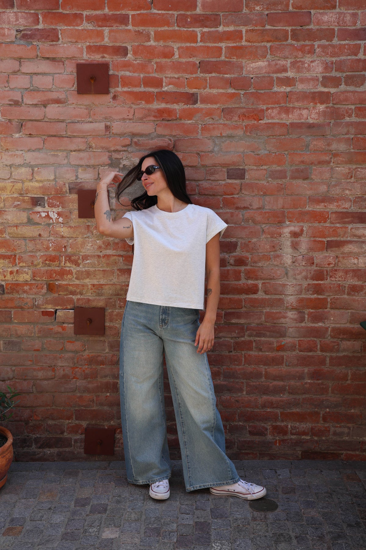 Woman wearing a great shirt with jeans against a brick wall.