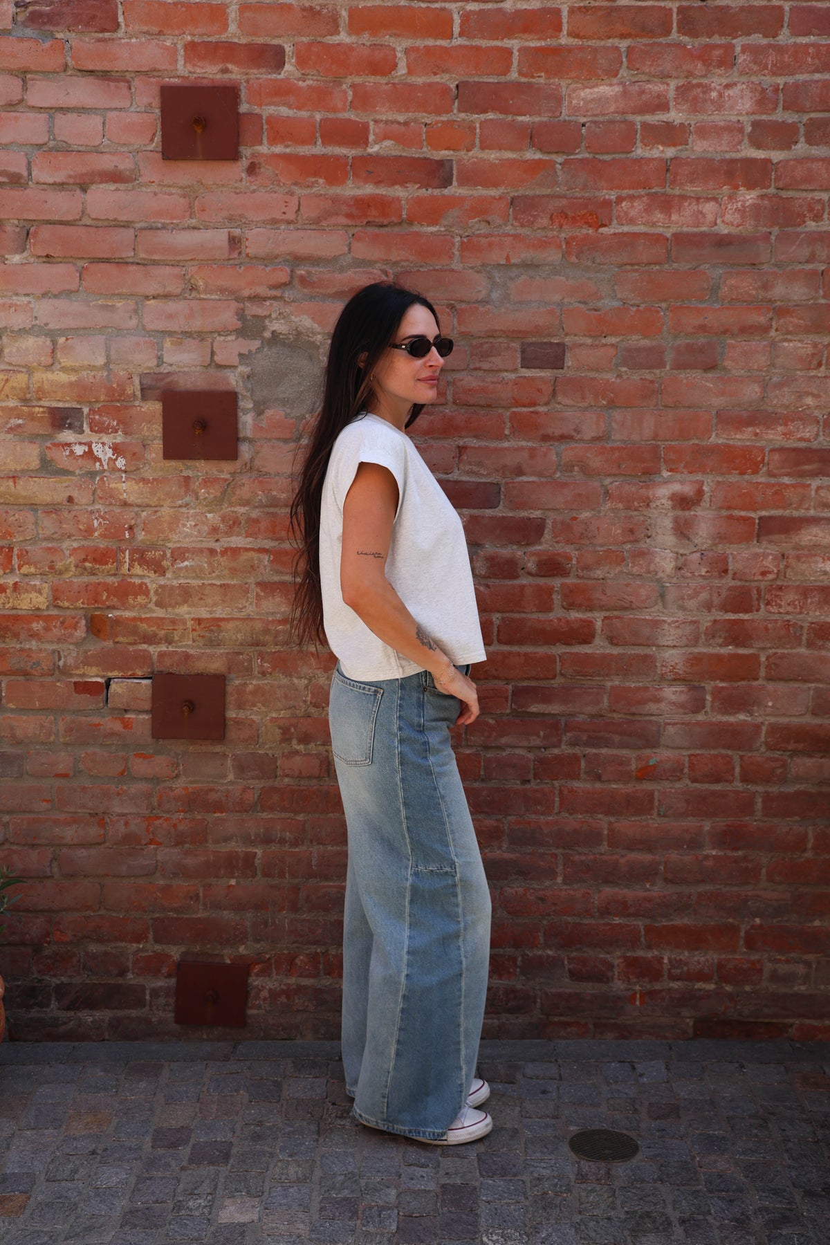 Woman wearing a great shirt with jeans against a brick wall.