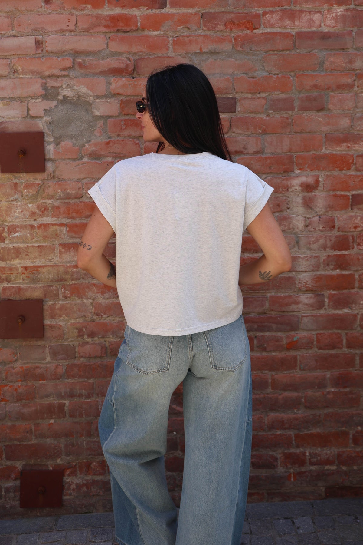 Woman wearing a great shirt with jeans against a brick wall.