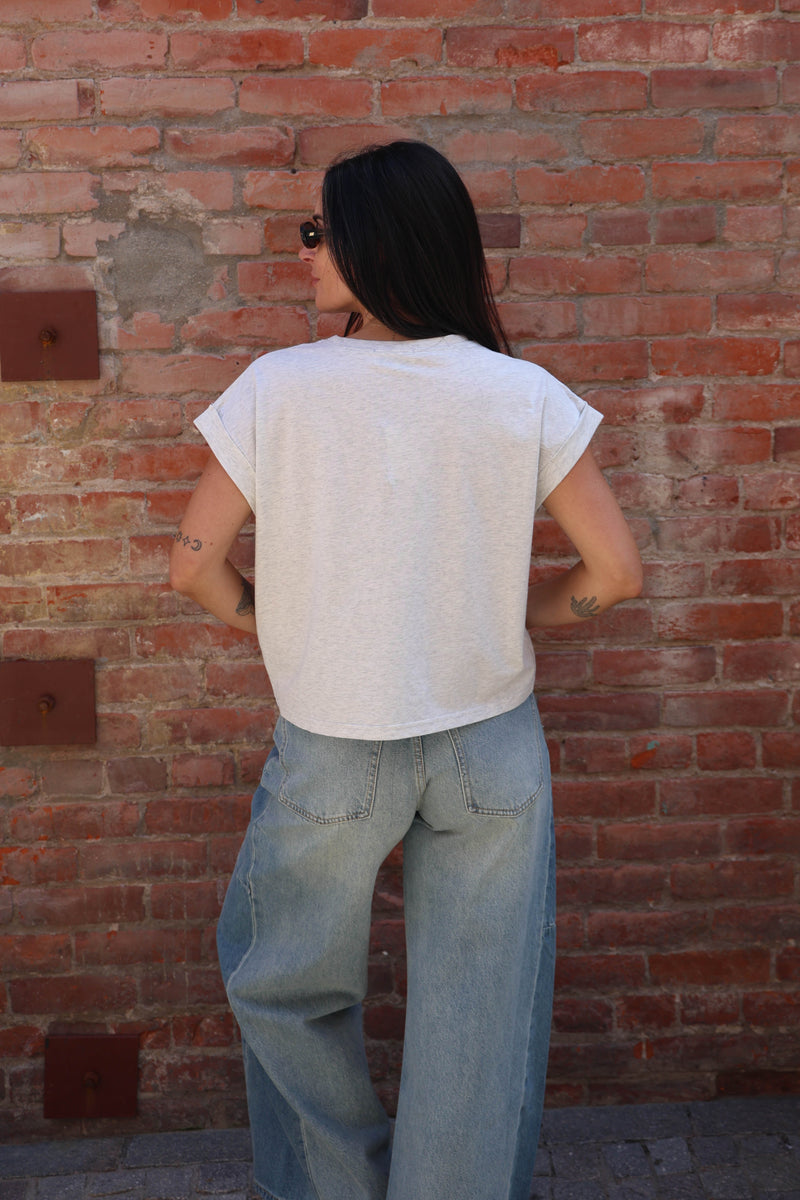 Woman wearing a great shirt with jeans against a brick wall.
