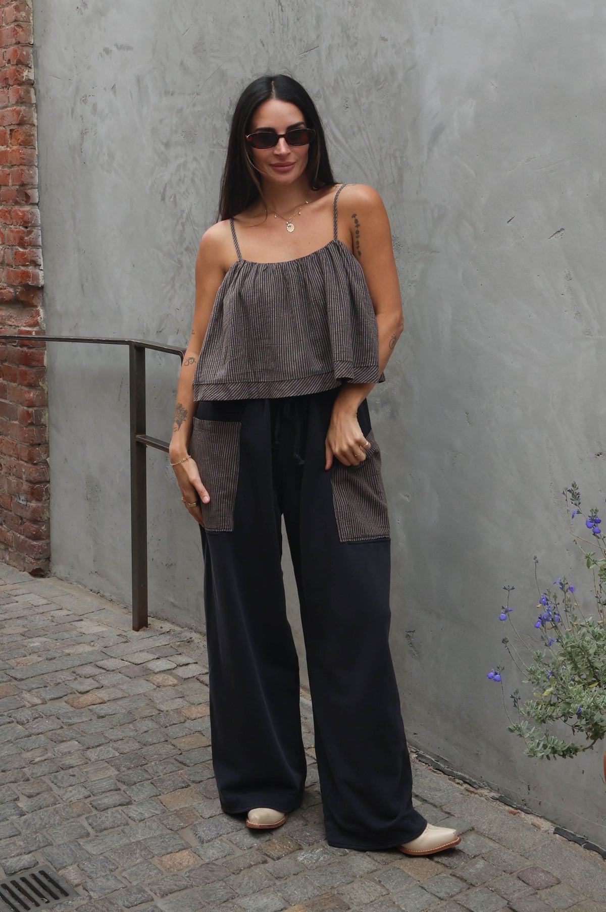 Woman in gray top and black pants standing against a gray wall with a brick column.
