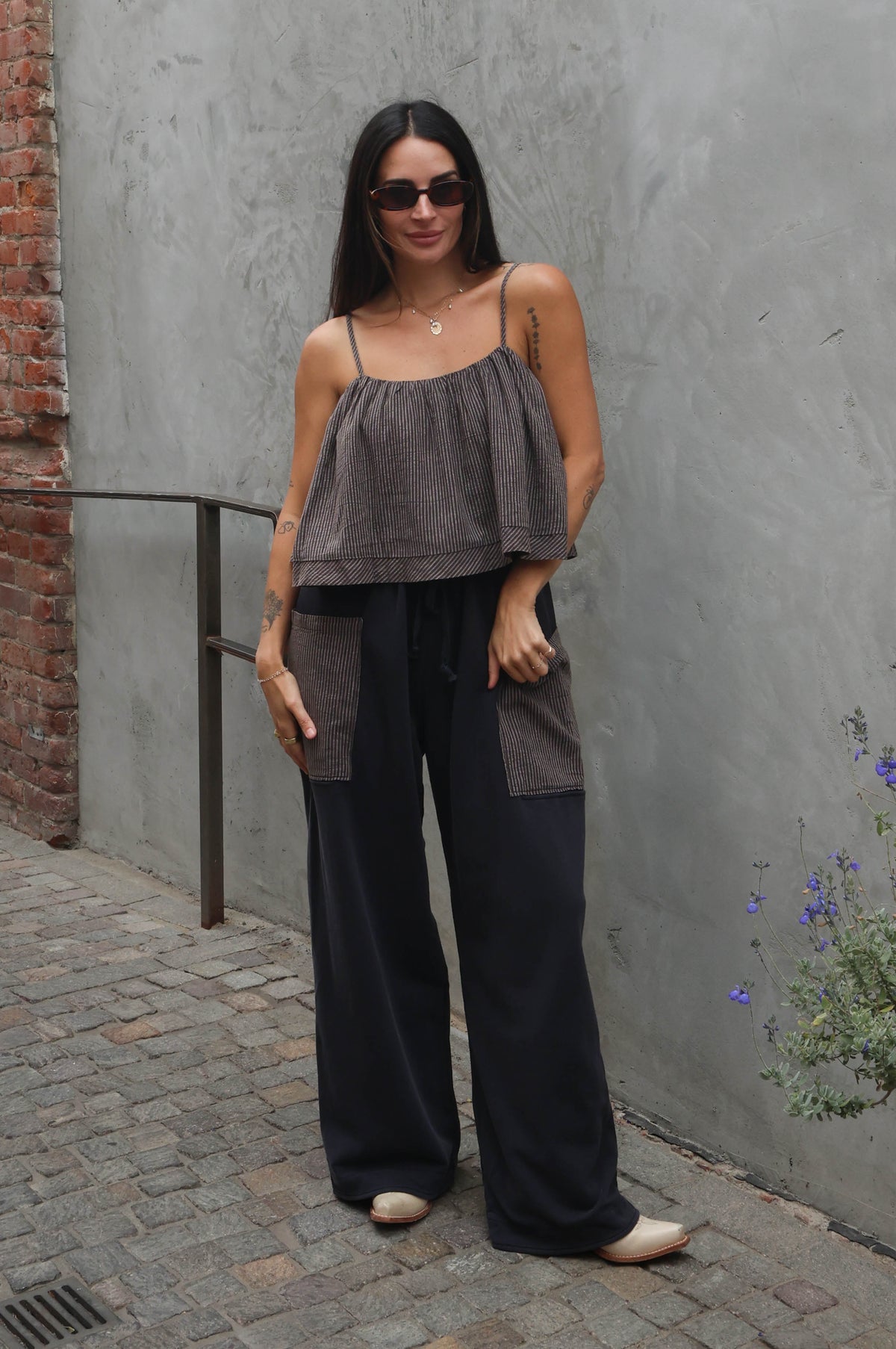 Woman in gray top and black pants standing against a gray wall with a brick column.