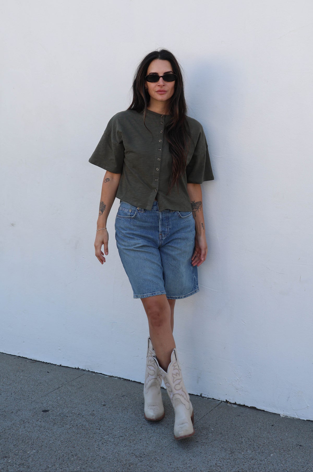 woman wearing a green shirt and jean shorts against a white background