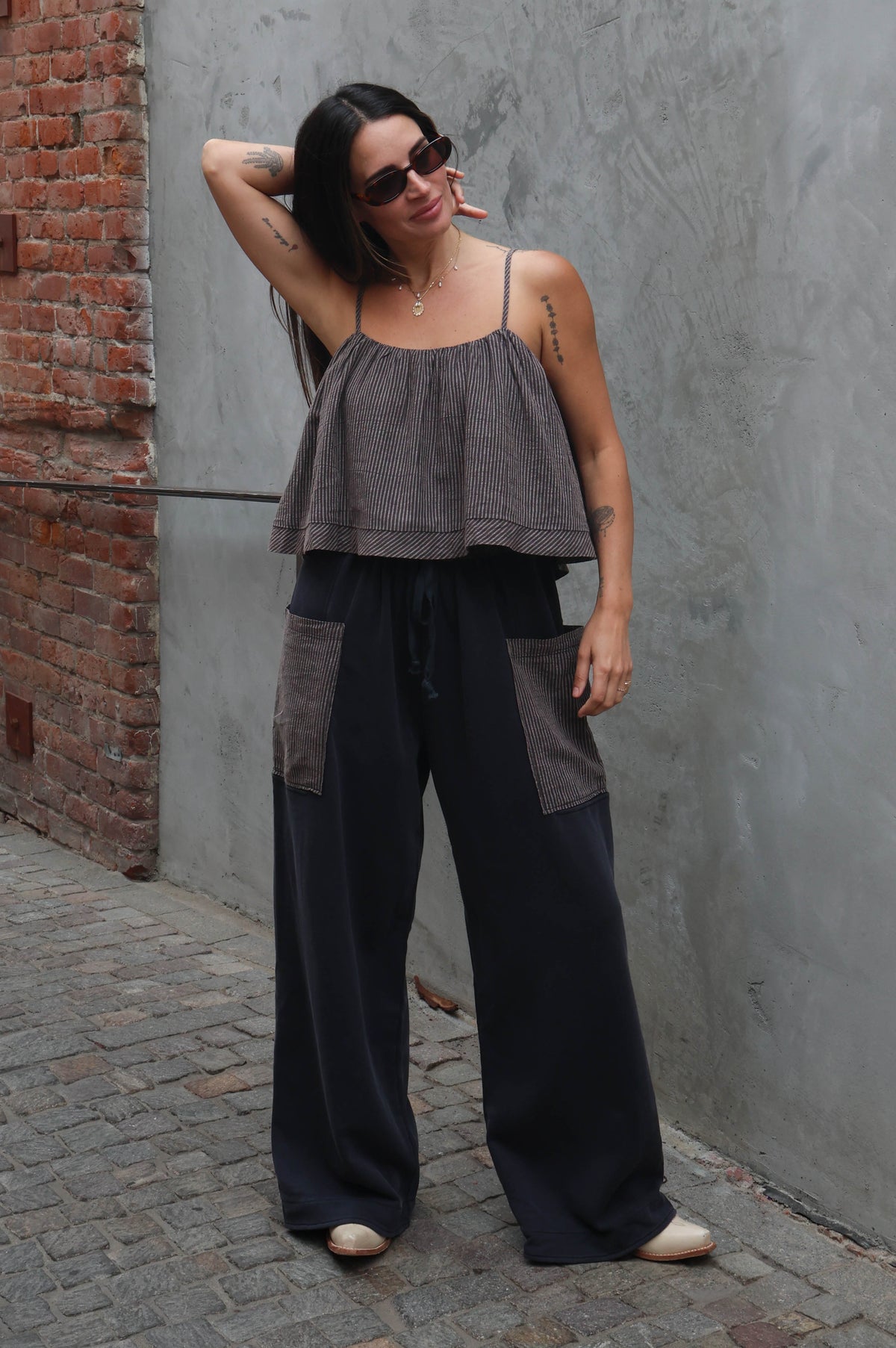 Woman in gray top and black pants standing against a gray wall.
