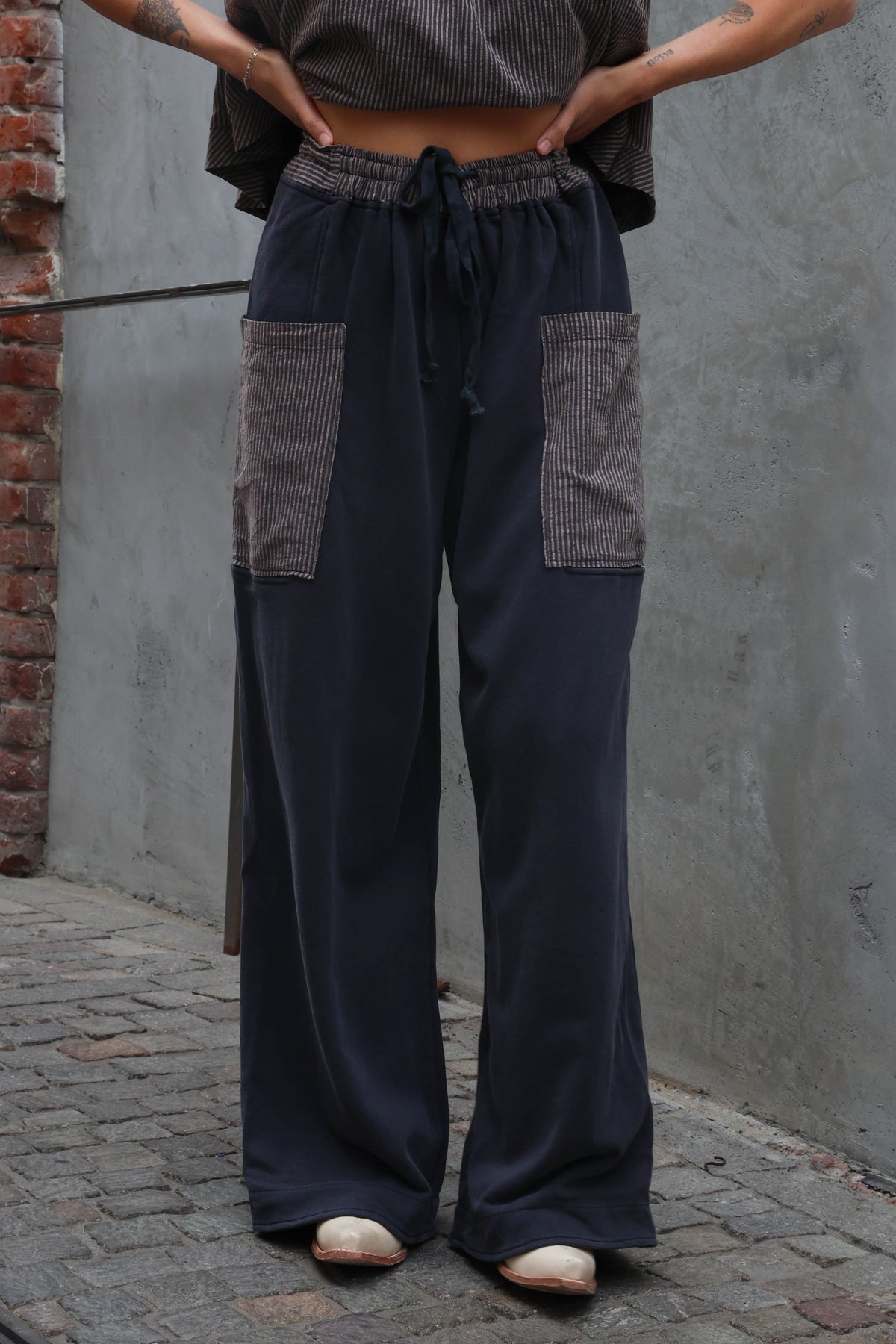 Person wearing dark blue wide-leg pants with patchwork details against a gray wall.