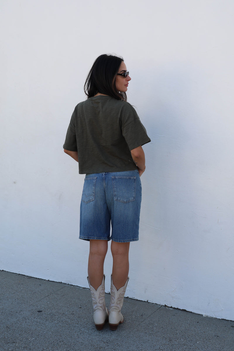 woman wearing a green shirt and jean shorts against a white background