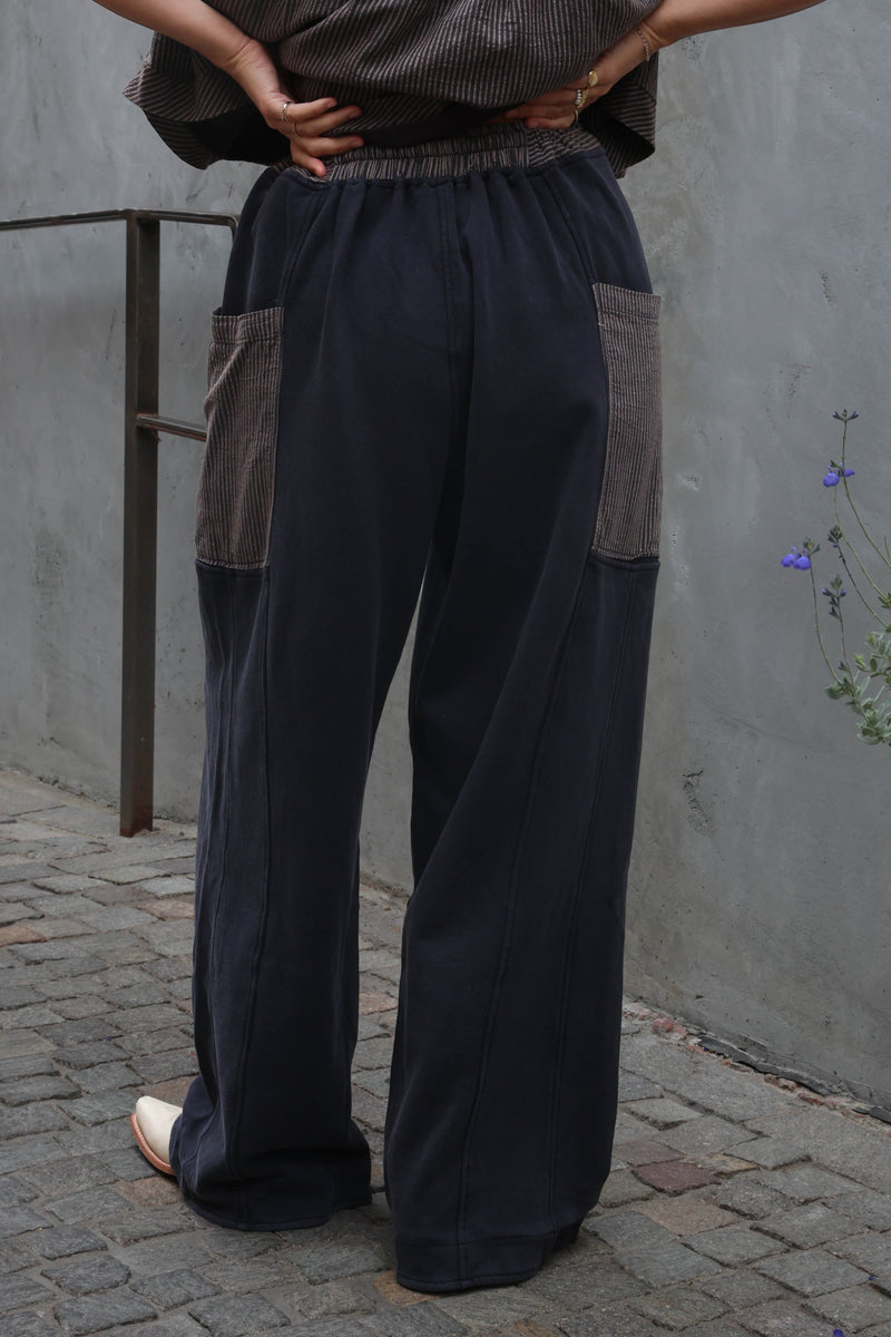 Person wearing dark blue wide-leg pants with brown accents against a gray wall.