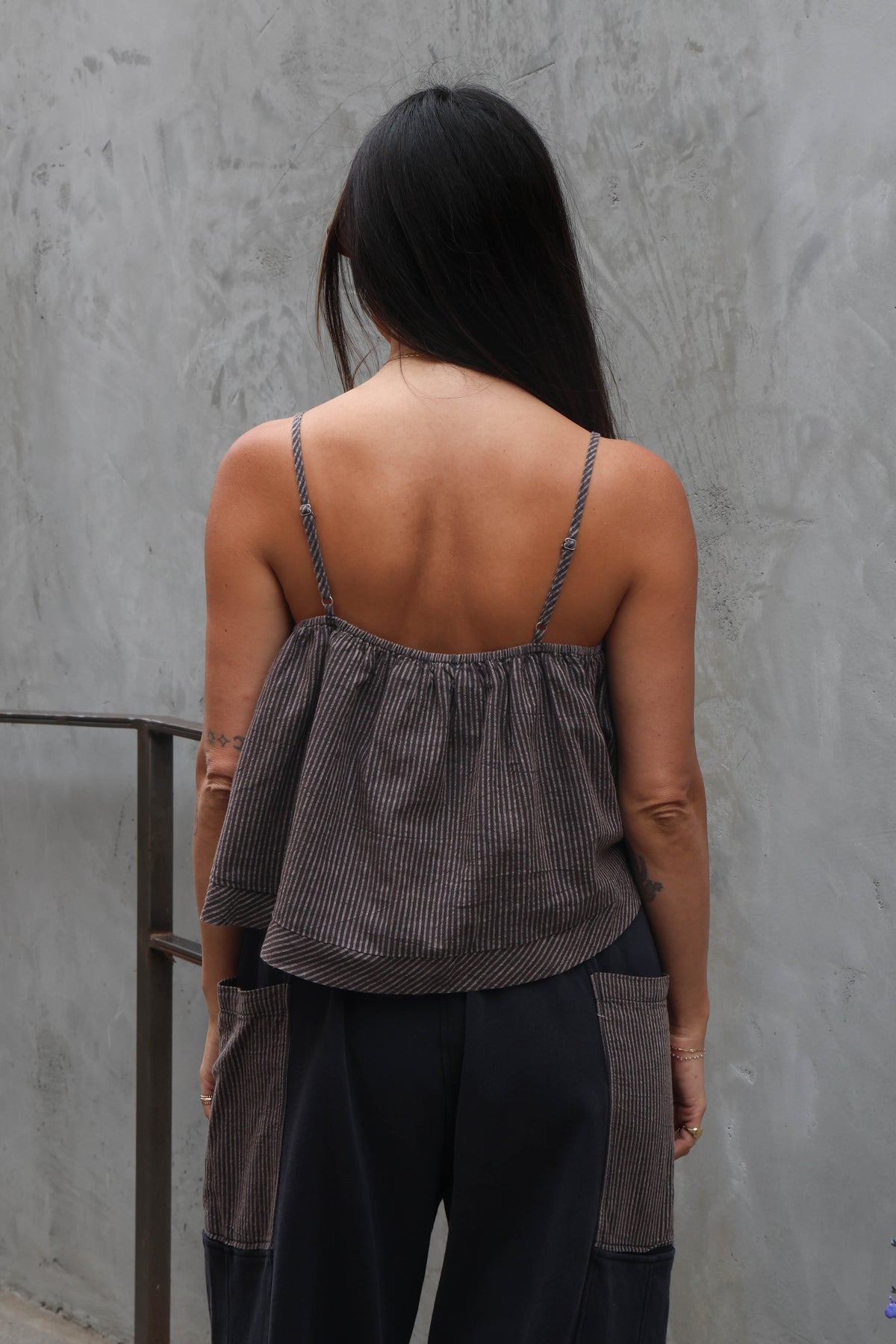 Person wearing a brown striped top and black pants against a gray wall.