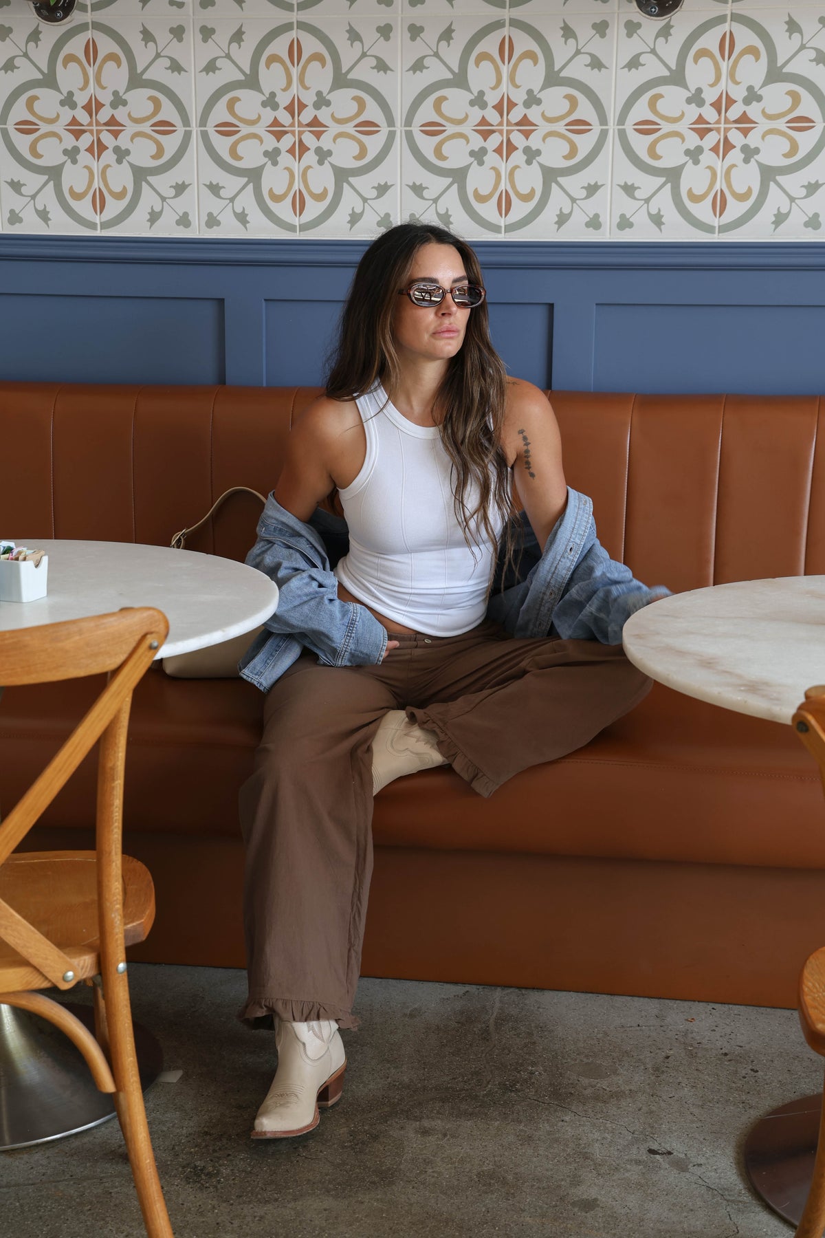 Woman sitting wearing brown pants with buttons holding a bag in a restaurant.