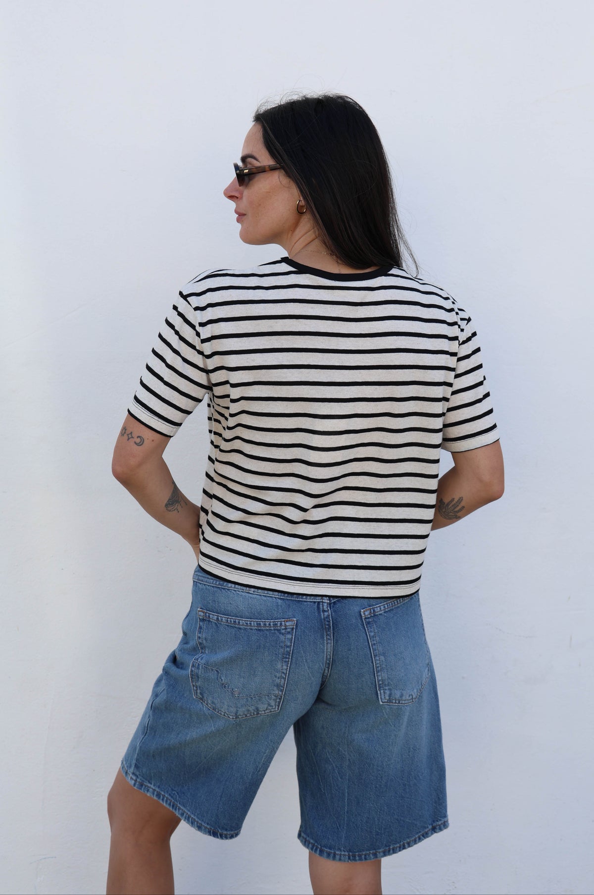 Woman wearing a striped t-shirt with jean shorts and boots against a white wall