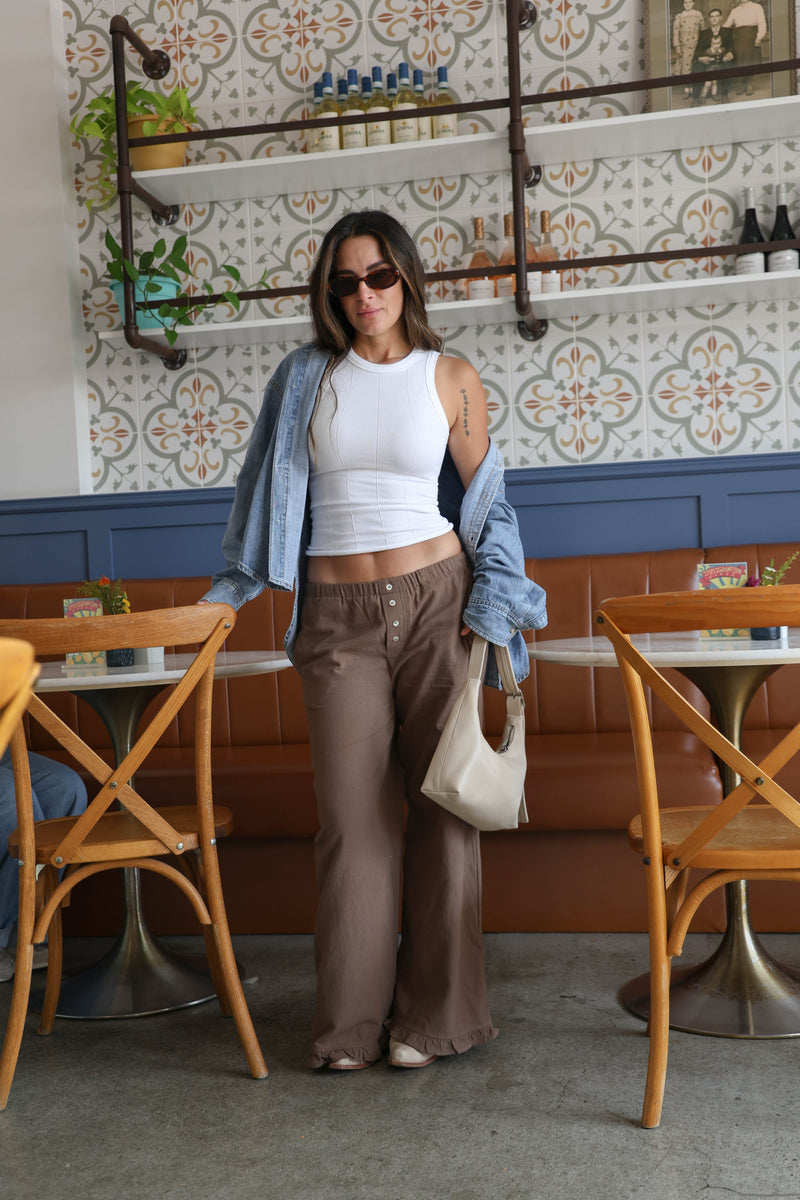 Woman wearing brown pants with buttons holding a bag in a restaurant.
