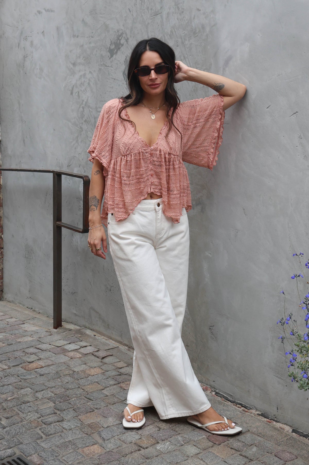Woman wearing a blush lace blouse against a grey wall