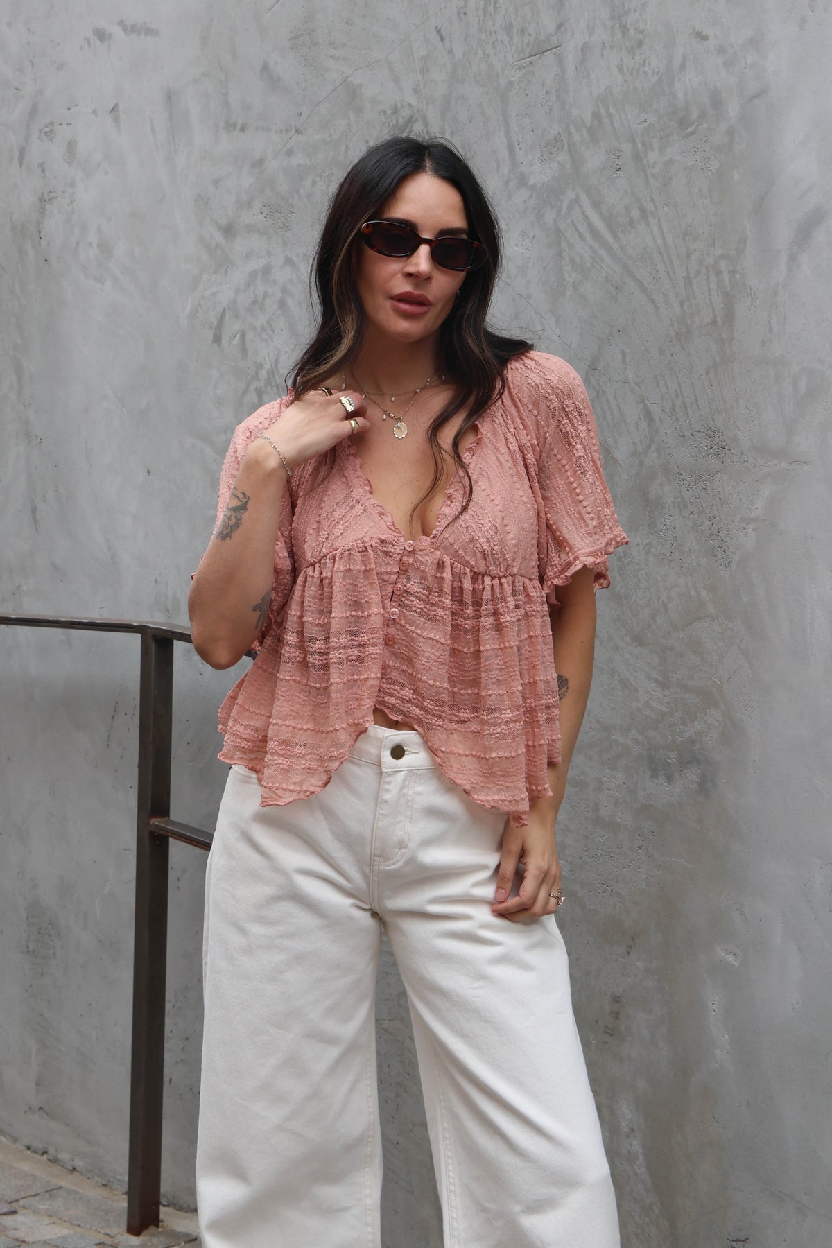 Woman wearing a blush lace blouse against a grey wall