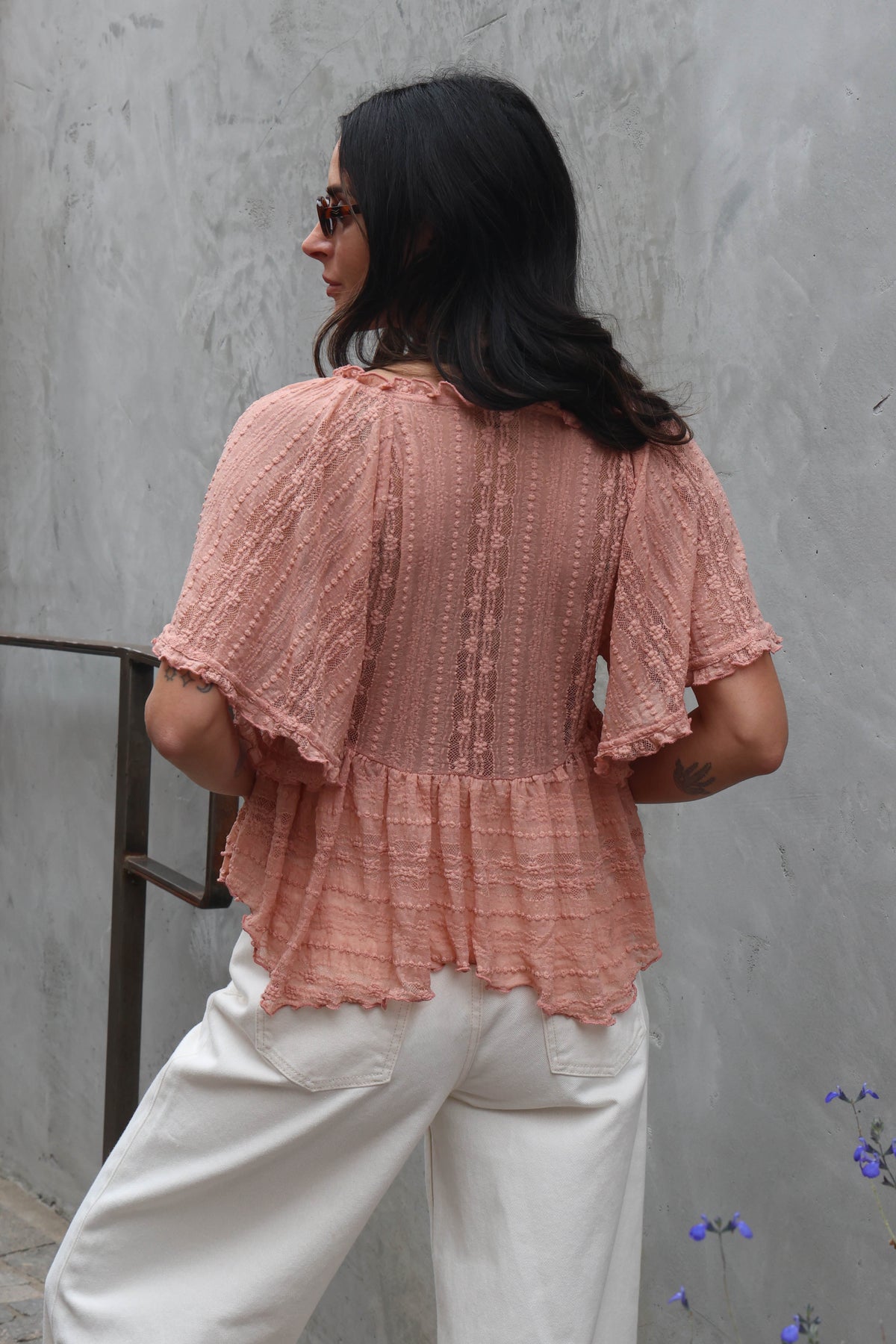 Woman wearing a blush lace blouse against a grey wall