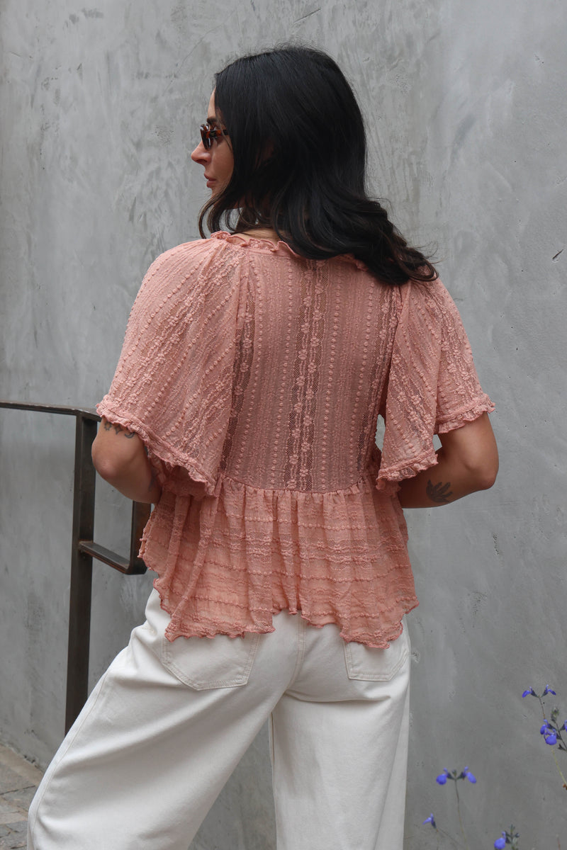Woman wearing a blush lace blouse against a grey wall