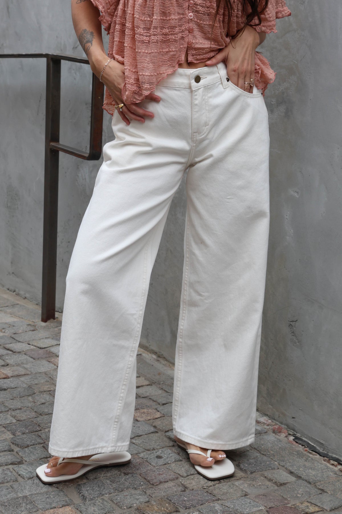 Woman wearing white jeans and a blush lace blouse against a brick wall