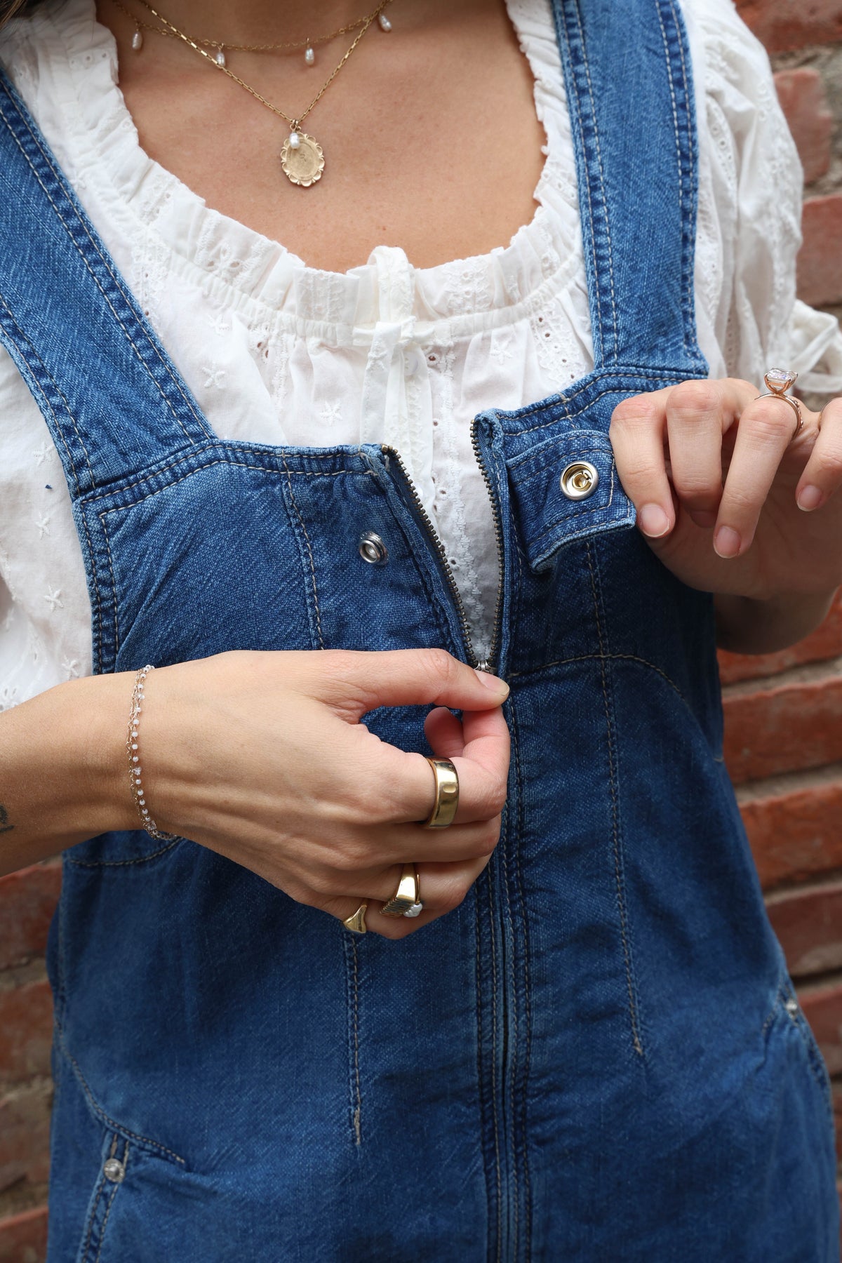 Woman wearing a pair of overalls with a white blouse against a brick wall