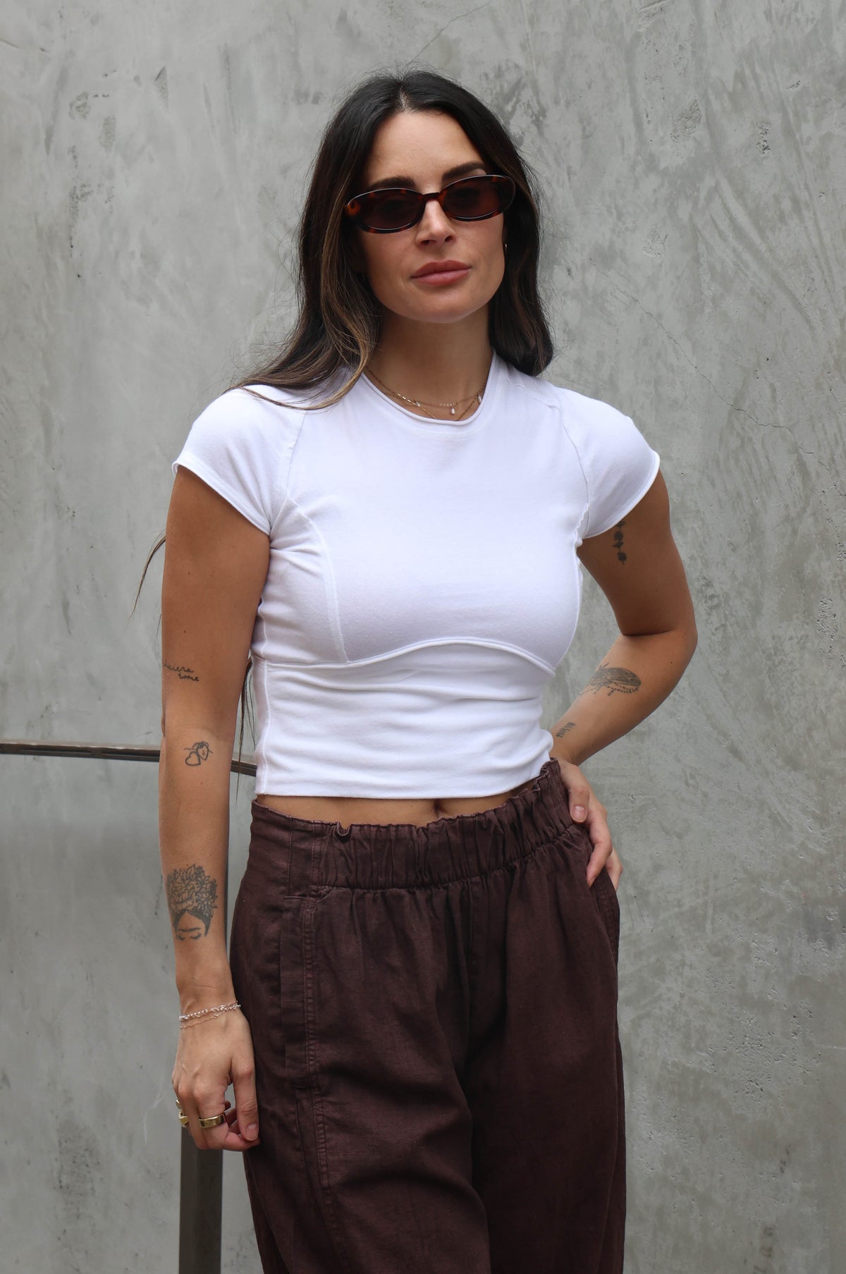 Woman wearing a white top and brown linen pants against a grey background