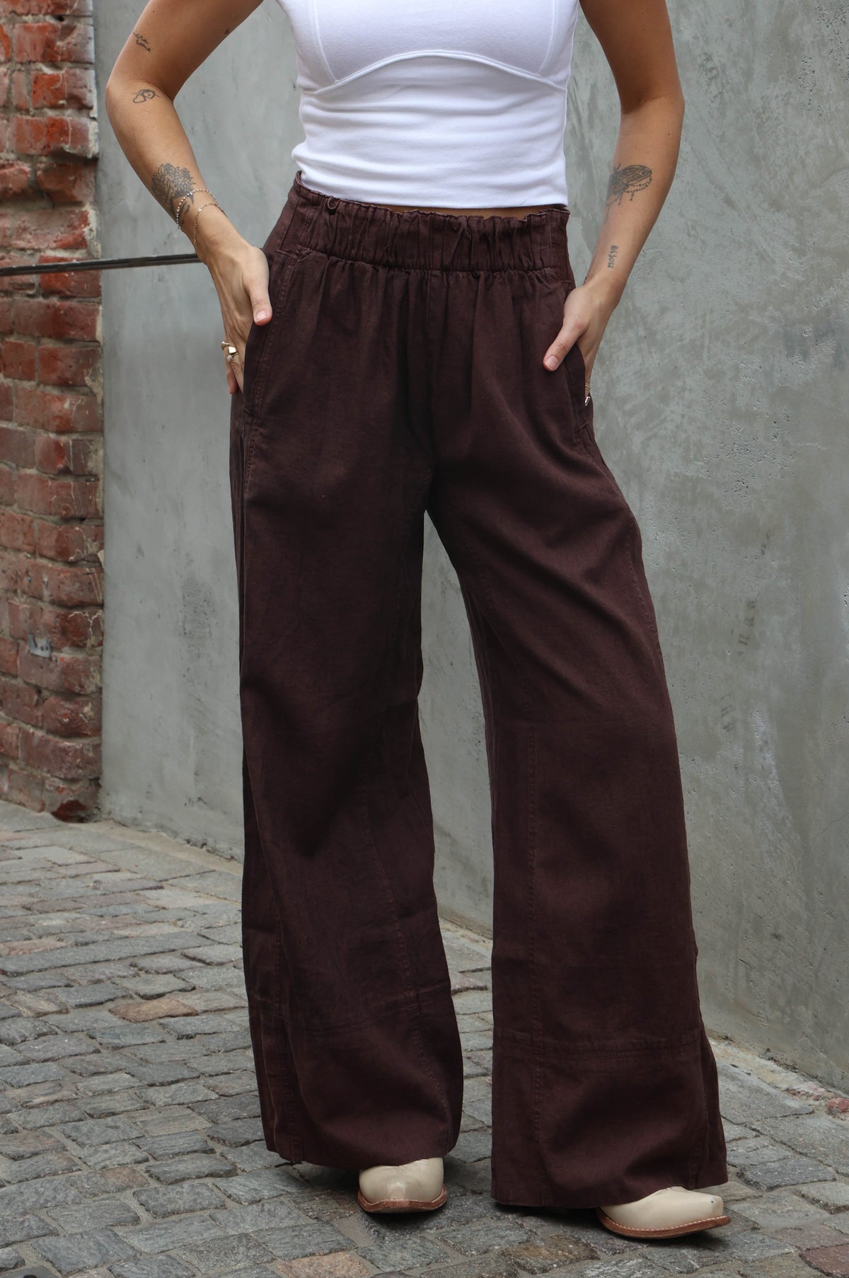 woman wearing brown linen pants against a grey background