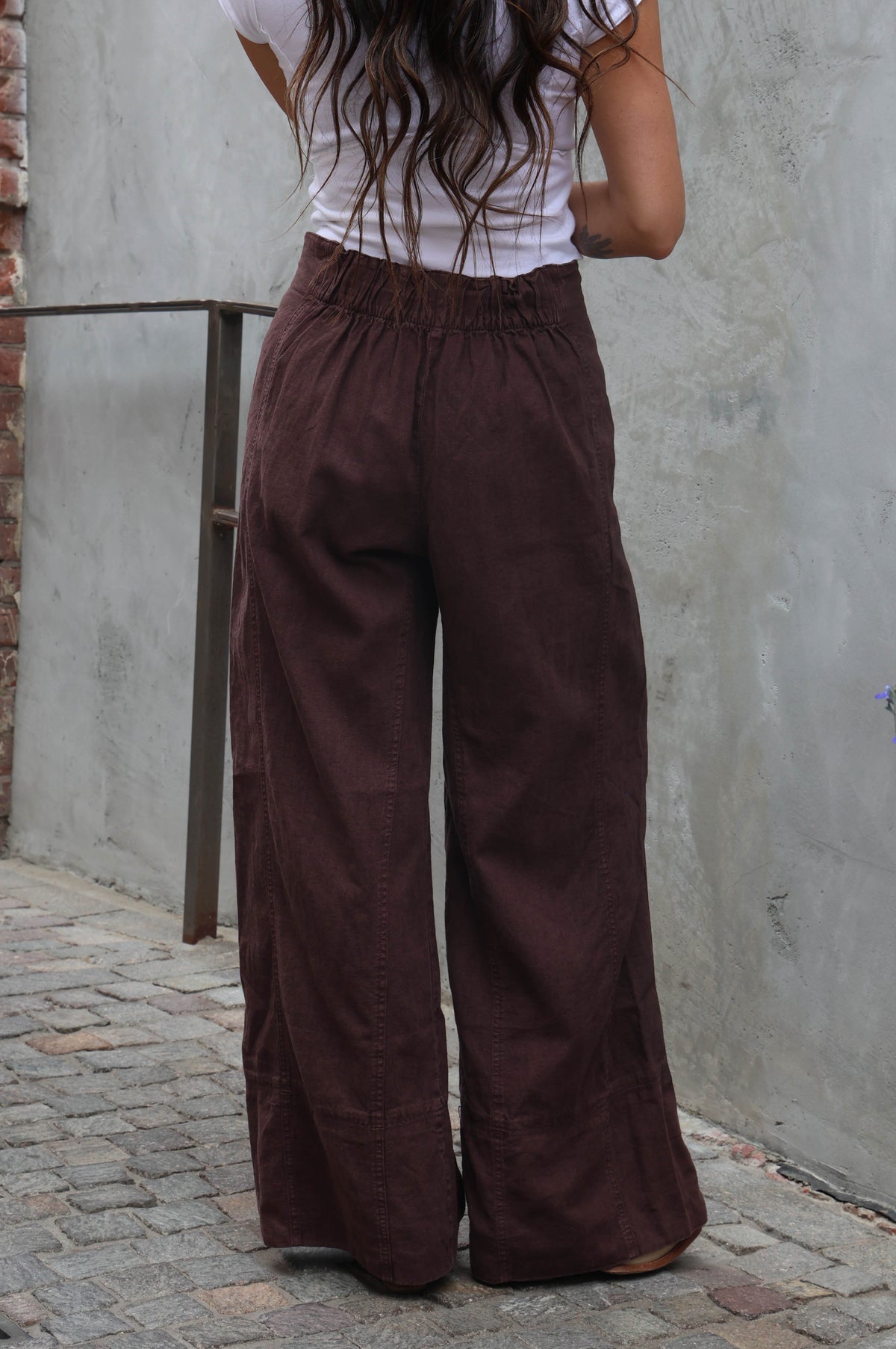woman wearing brown linen pants against a grey background